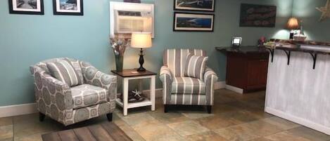 Un salon comprenant un fauteuil à motifs, un fauteuil à rayures, une table basse en bois et une petite table d’appoint avec une lampe.