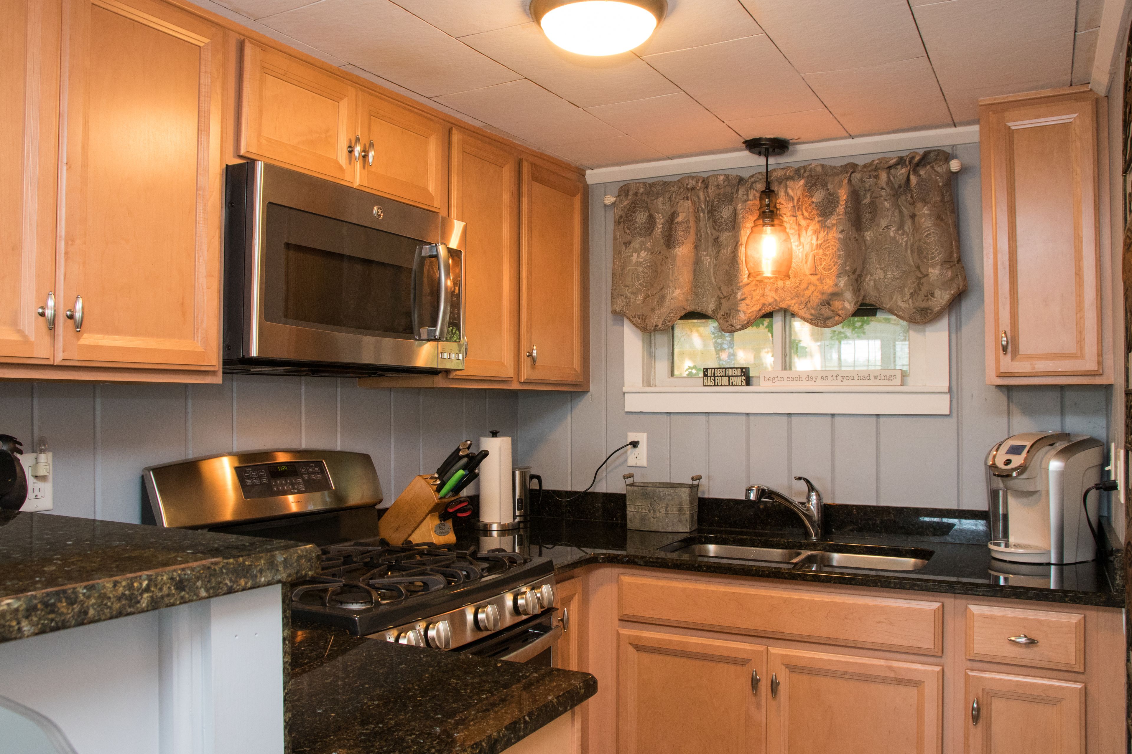 A kitchen with wooden cabinets, stainless steel appliances, granite countertops, and a window with decorative curtains.