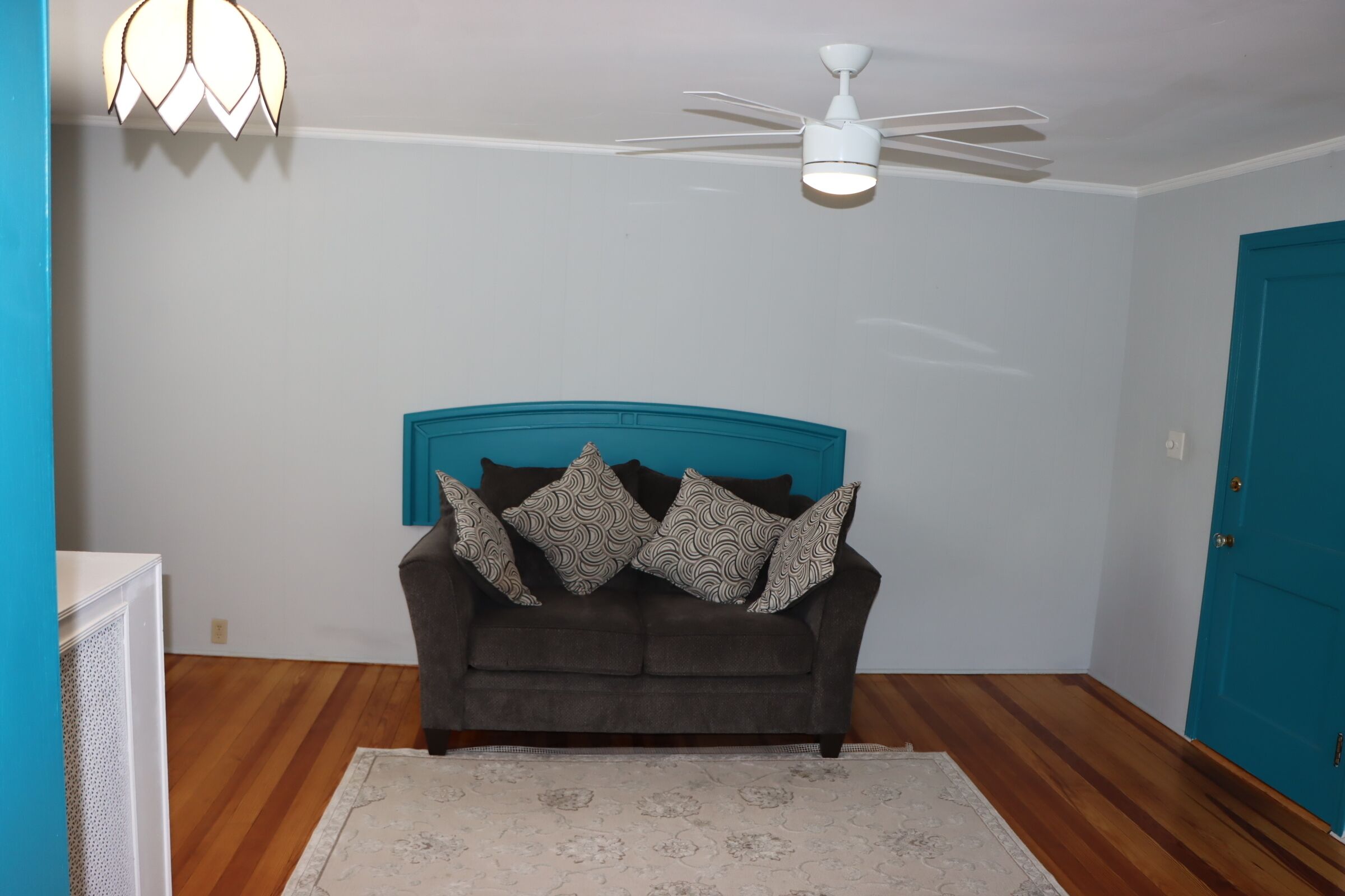 A room with a dark brown sofa, patterned cushions, a white ceiling fan, and a teal door.