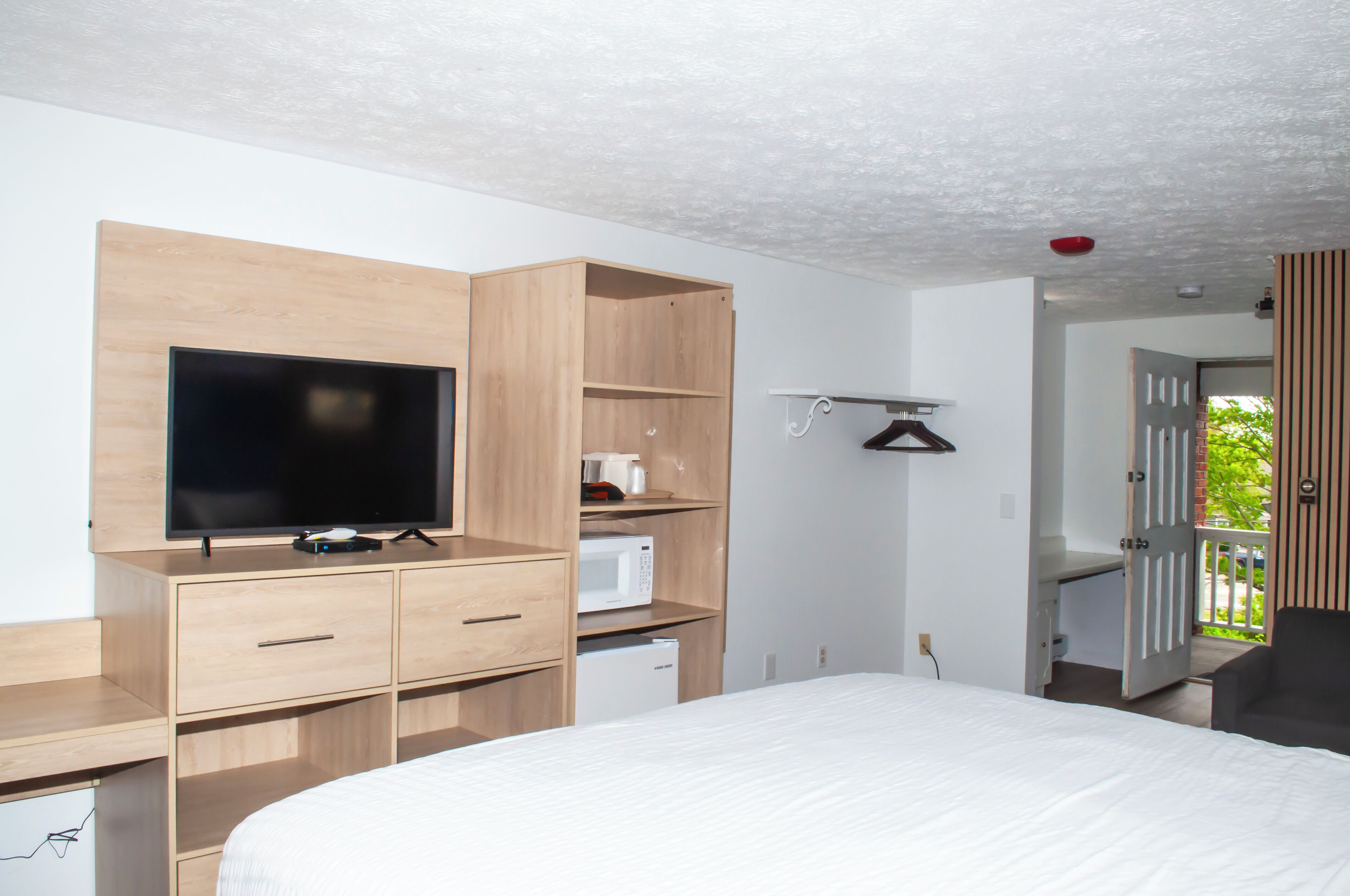 A modern hotel room with a large bed, a flat-screen TV, a microwave, and a small refrigerator.