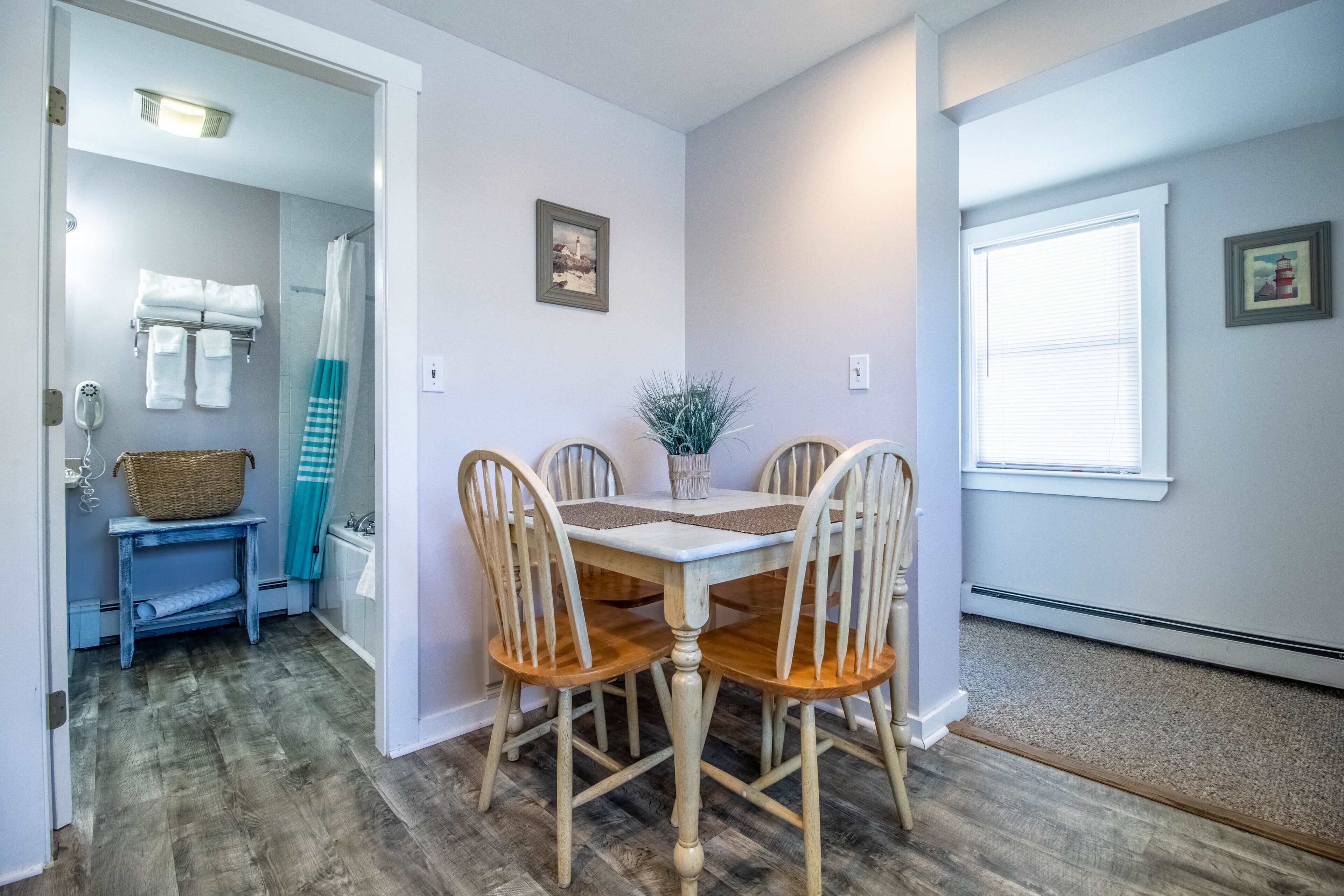 A dining area with a table and chairs, a basket on a small table, and a shower area with towels and a basket.