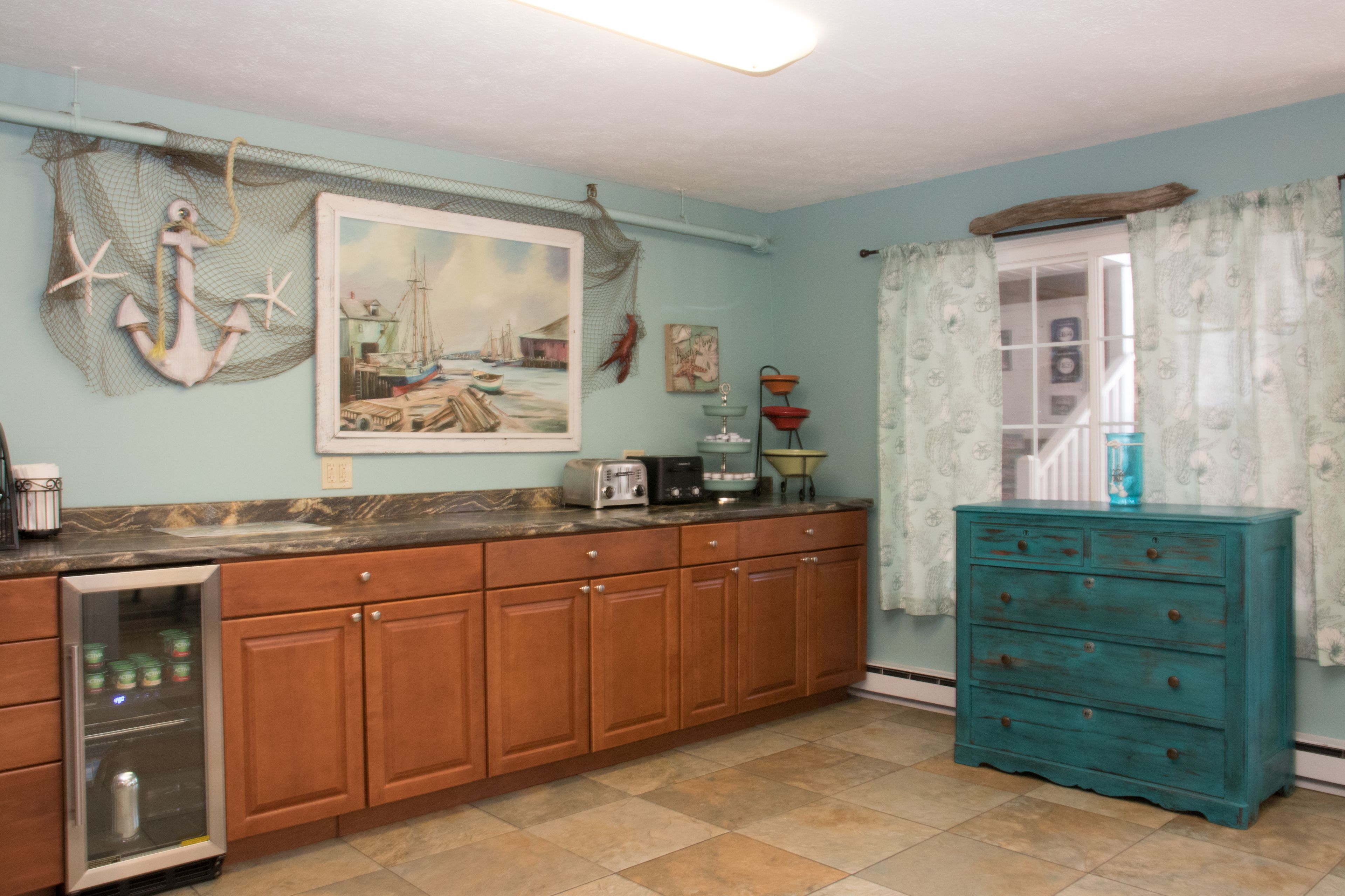 A kitchen with wooden cabinets, a teal dresser, and a painting of a harbor scene.