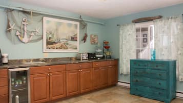 A kitchen with wooden cabinets, a teal dresser, and a painting of a harbor scene.