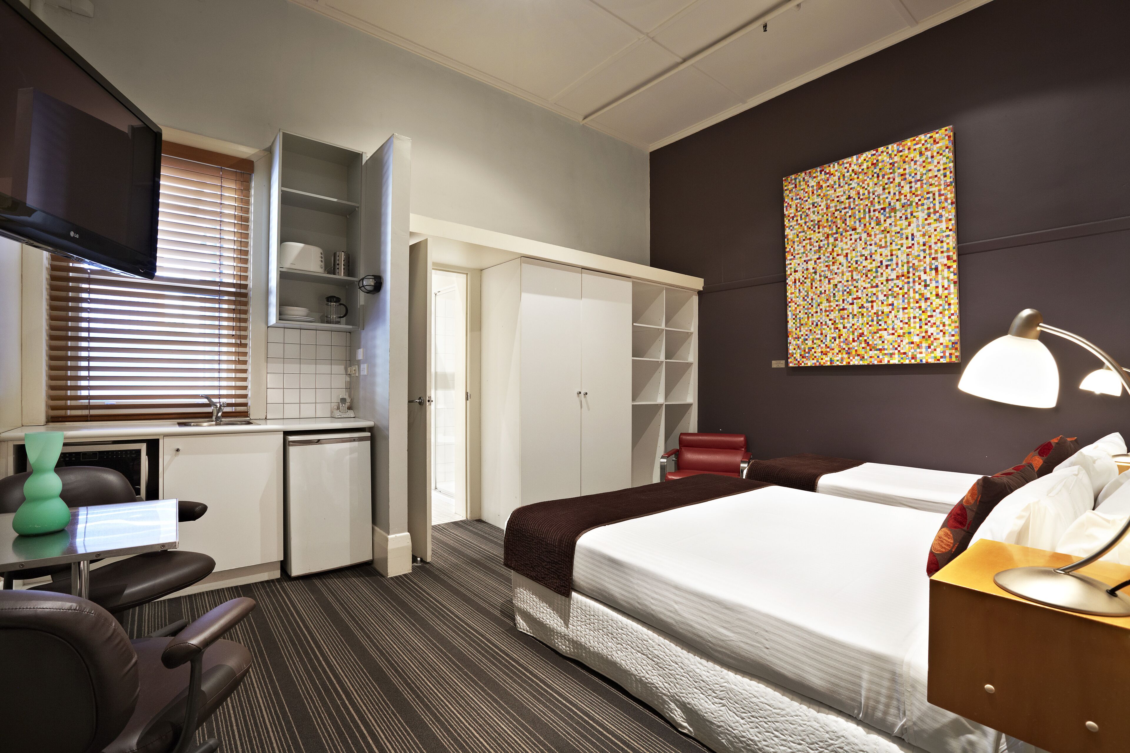Una habitación de hotel con cama, escritorio con silla, televisor y armario.