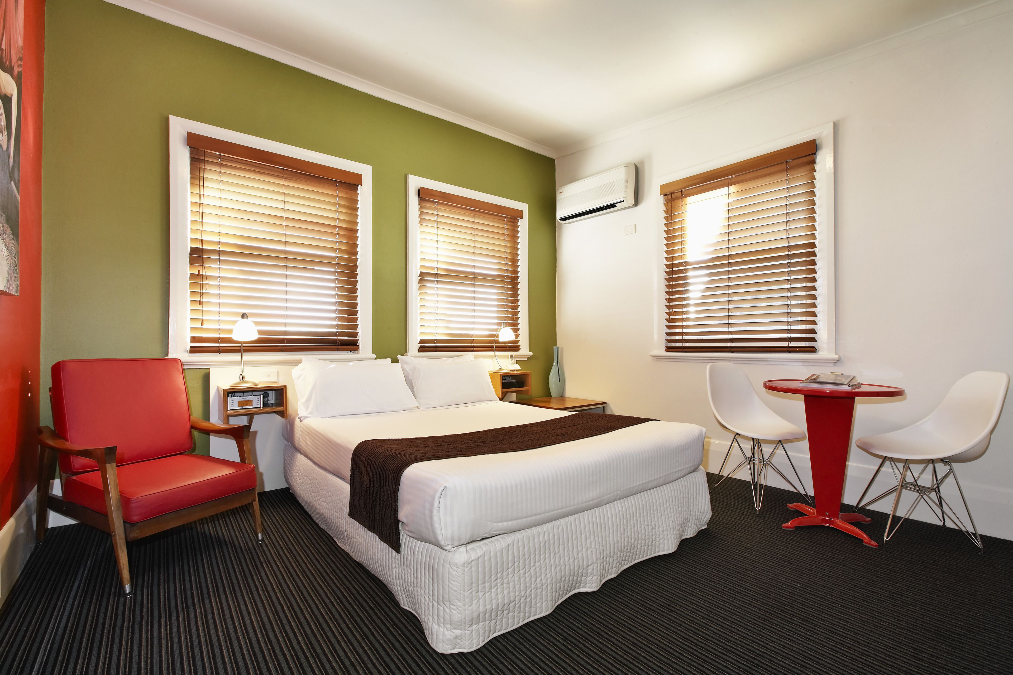Een hotelkamer met een bed, een rode fauteuil, een tafeltje en twee witte stoelen.