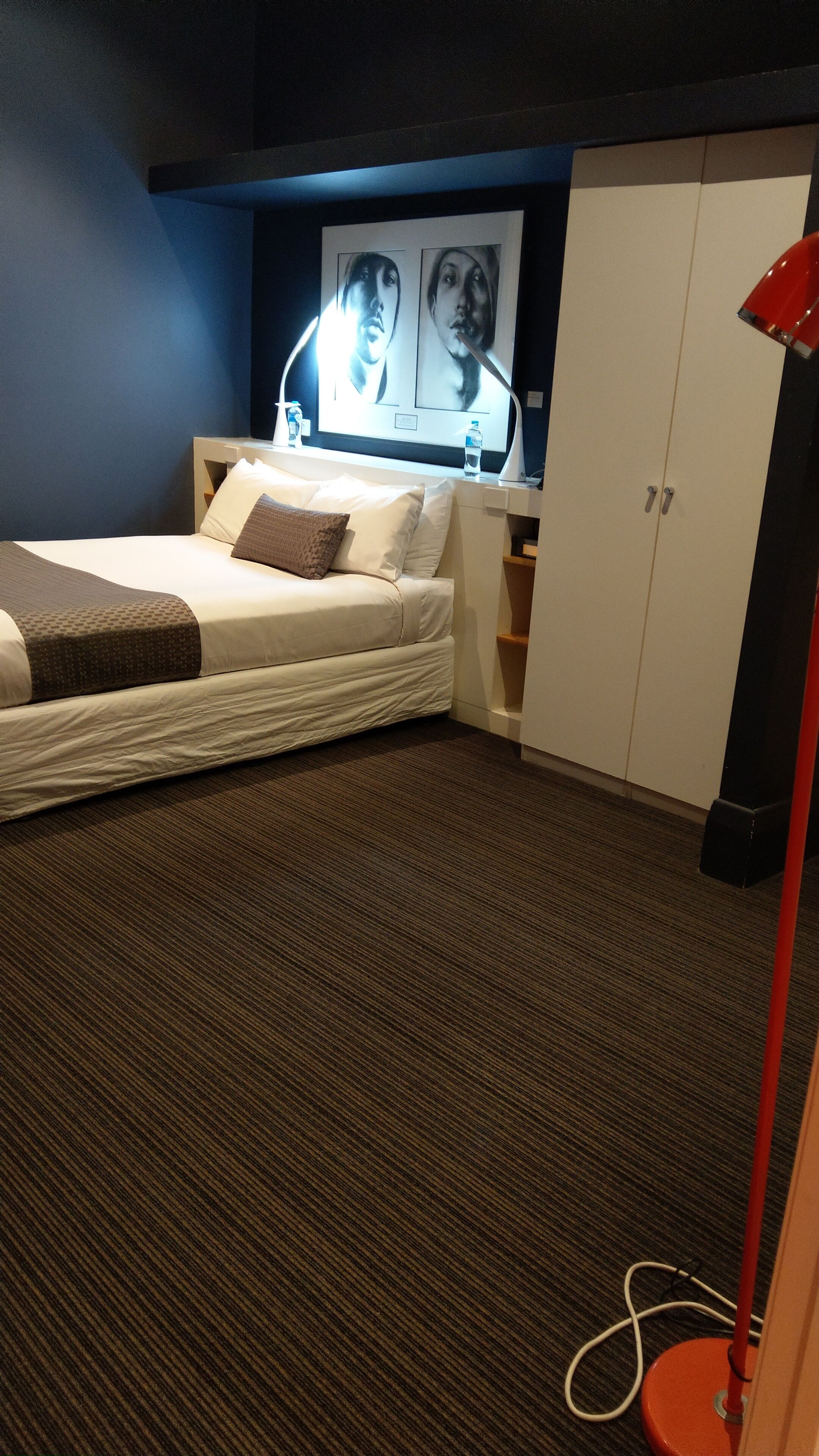 A hotel room with a bed, a desk, a wardrobe, and a wall-mounted TV.