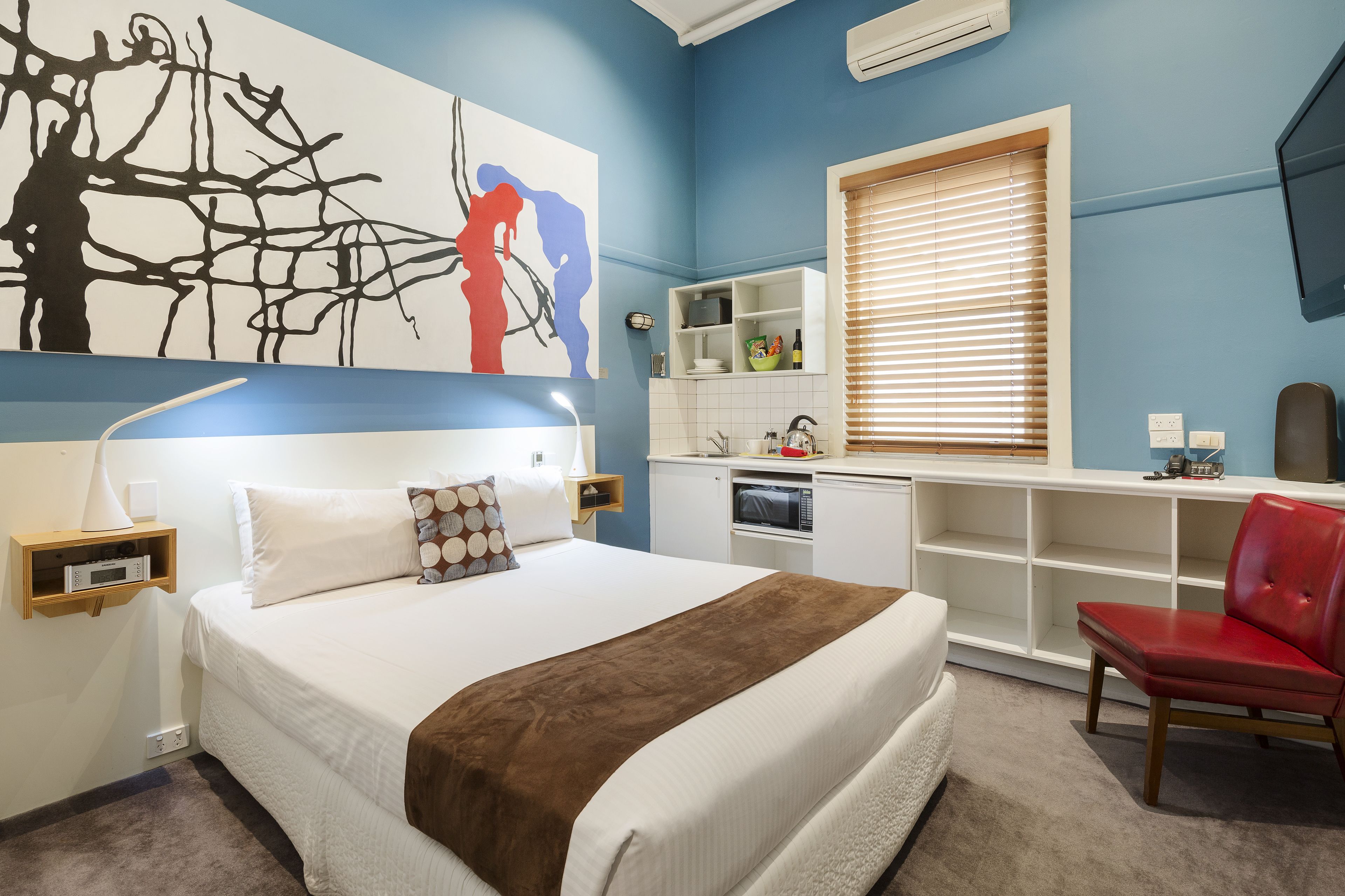 Un dormitorio con cama, una silla roja, un televisor y una kitchenette.
