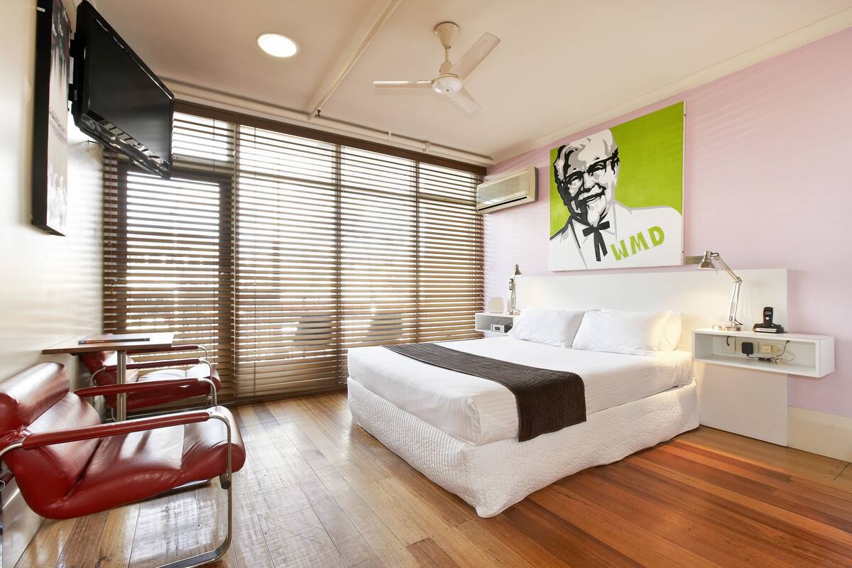 A hotel room with a bed, a desk, a chair, and a TV mounted on the wall.