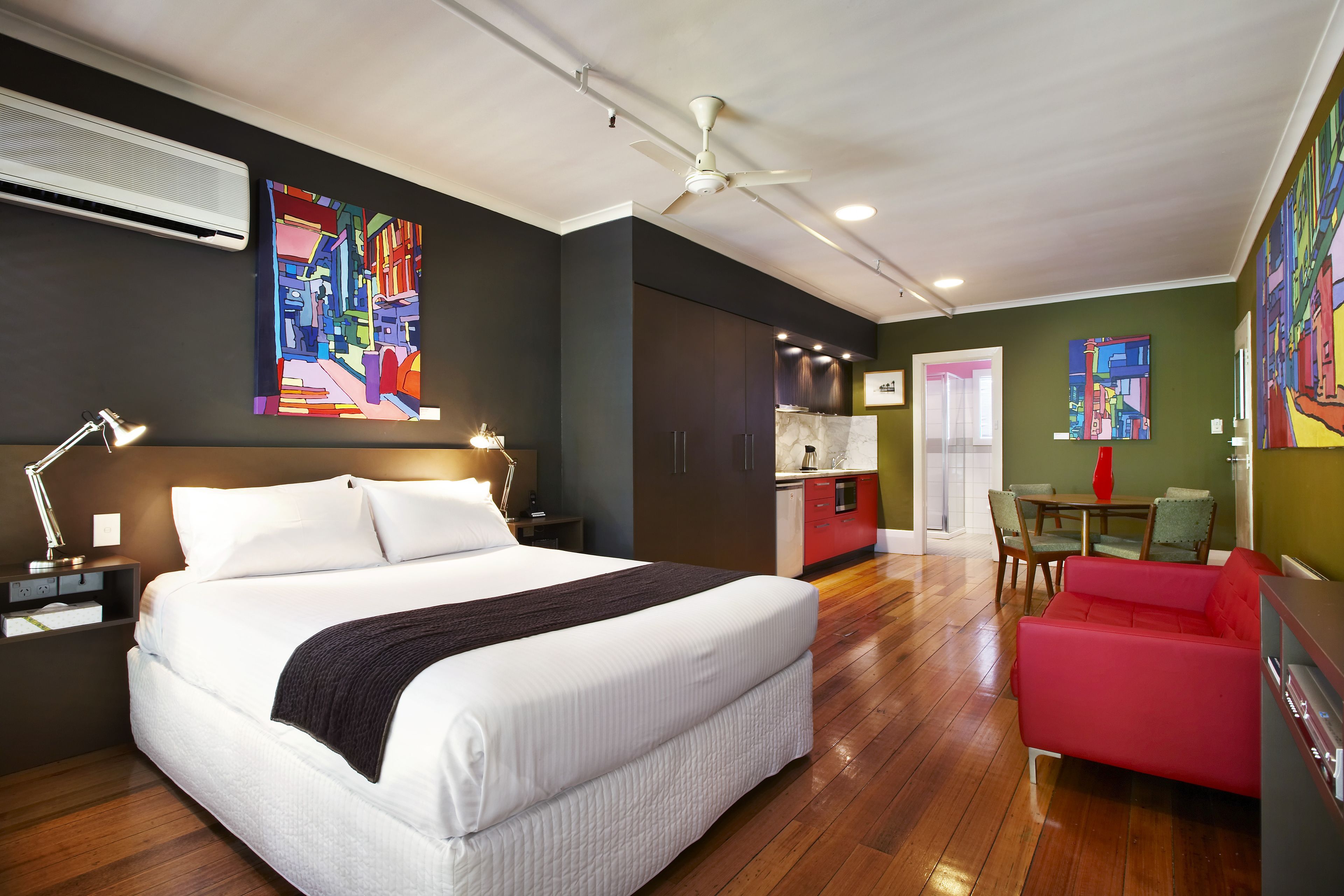 Una habitación de hotel moderna con una cama grande, un sofá rojo, un área de comedor y obras de arte en las paredes.