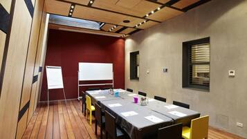 A conference room with a long table, chairs, a whiteboard, and a window with blinds.