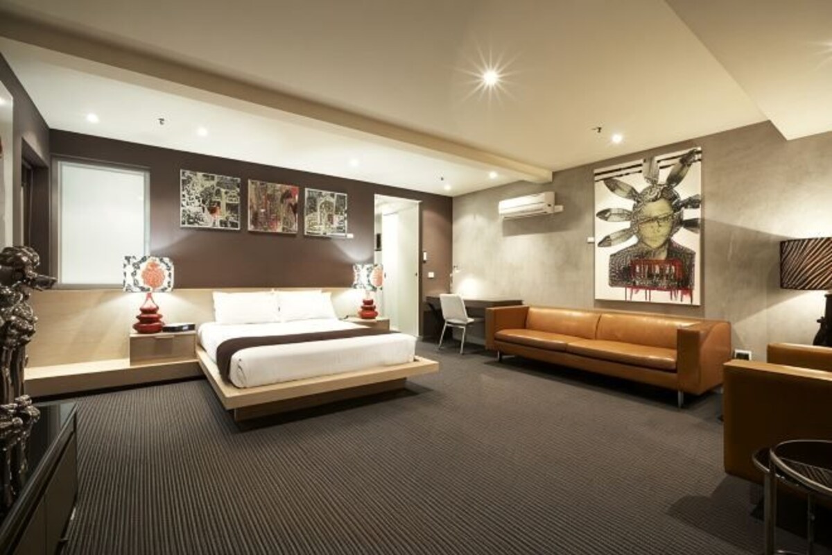 A modern hotel room with a bed, a sofa, a desk, and artwork on the walls.