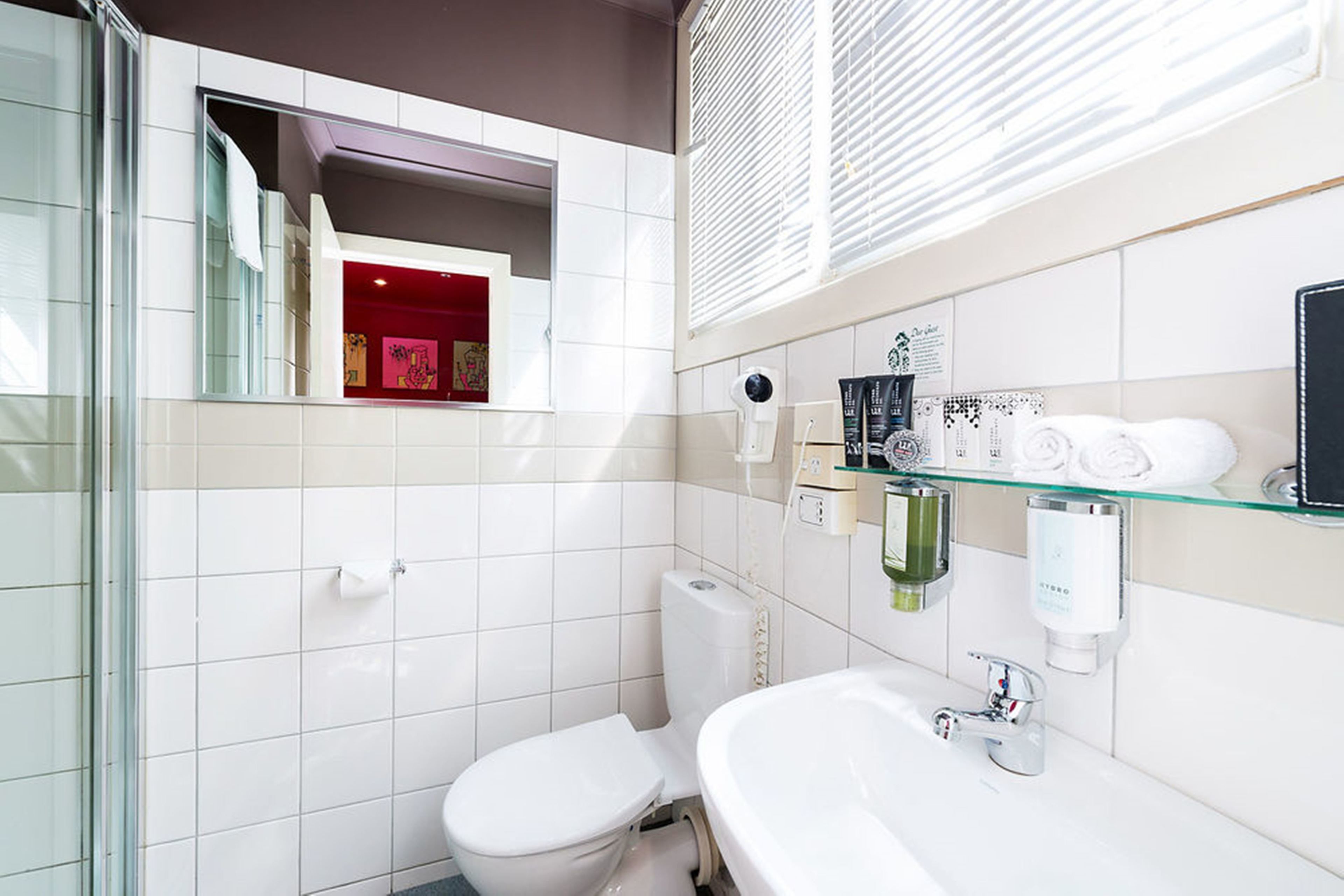 Ein modernes Badezimmer mit Duschkabine aus Glas, einer weißen Toilette, einem Waschbecken mit Glasablage und einem Spiegel darüber.
