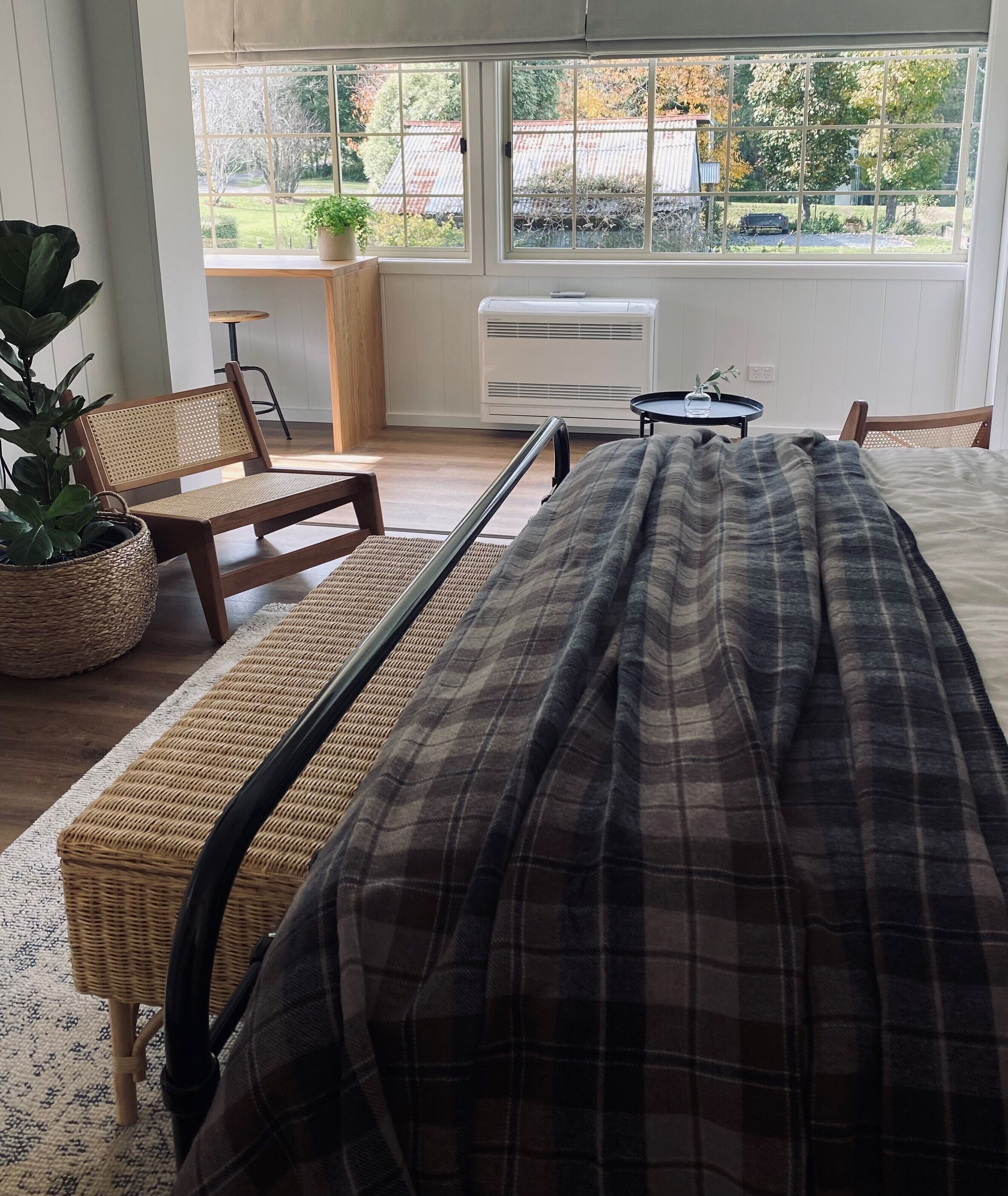 A bedroom with a bed, a chair, a small table, and a potted plant.