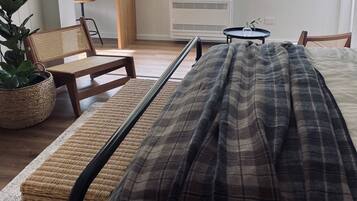 A bedroom with a bed, a chair, a small table, and a potted plant.