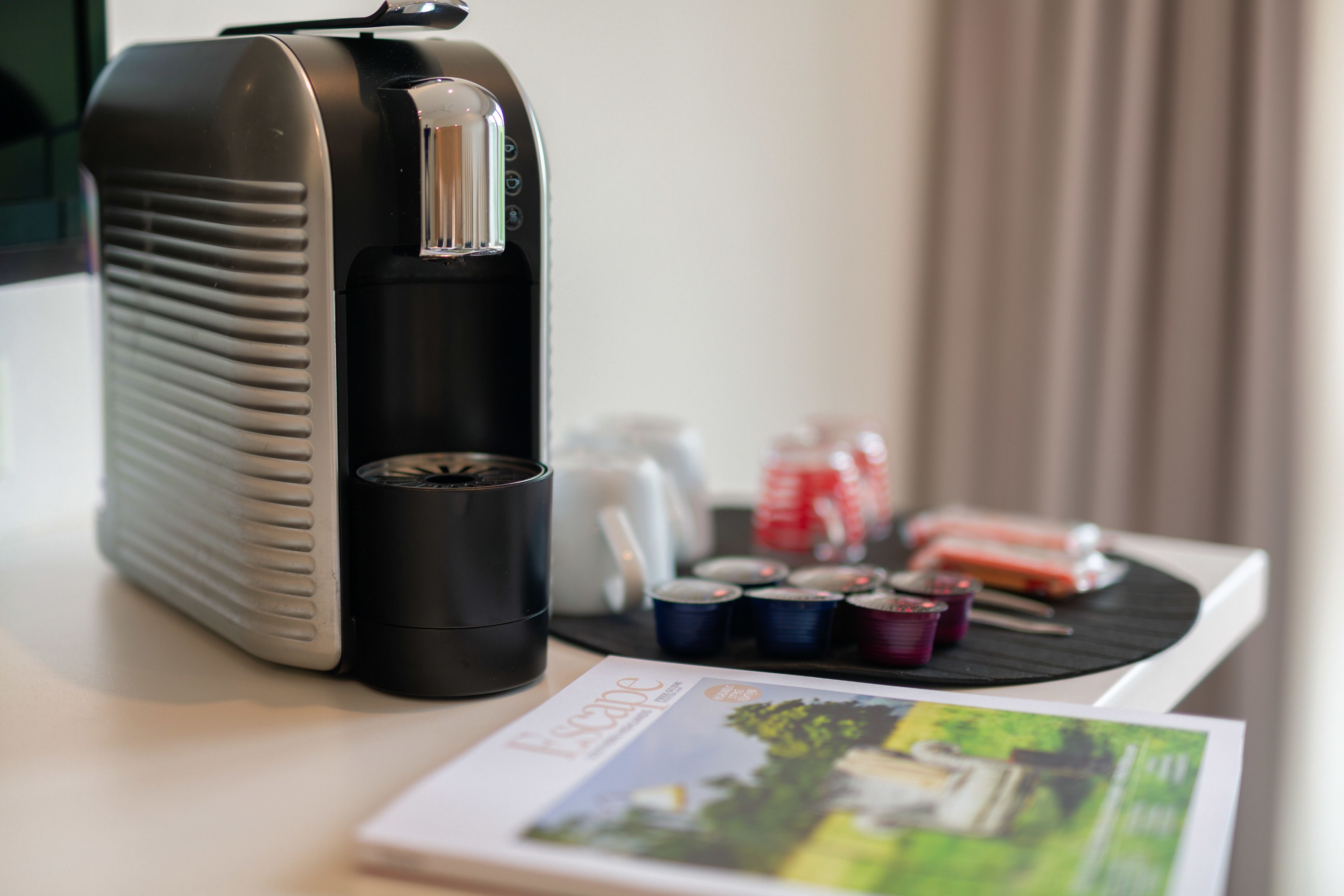 A coffee maker, a magazine, and some small containers on a table.