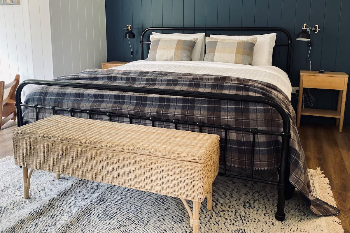 A bedroom with a bed, two bedside tables, a nightstand, a wicker bench, and a patterned rug.