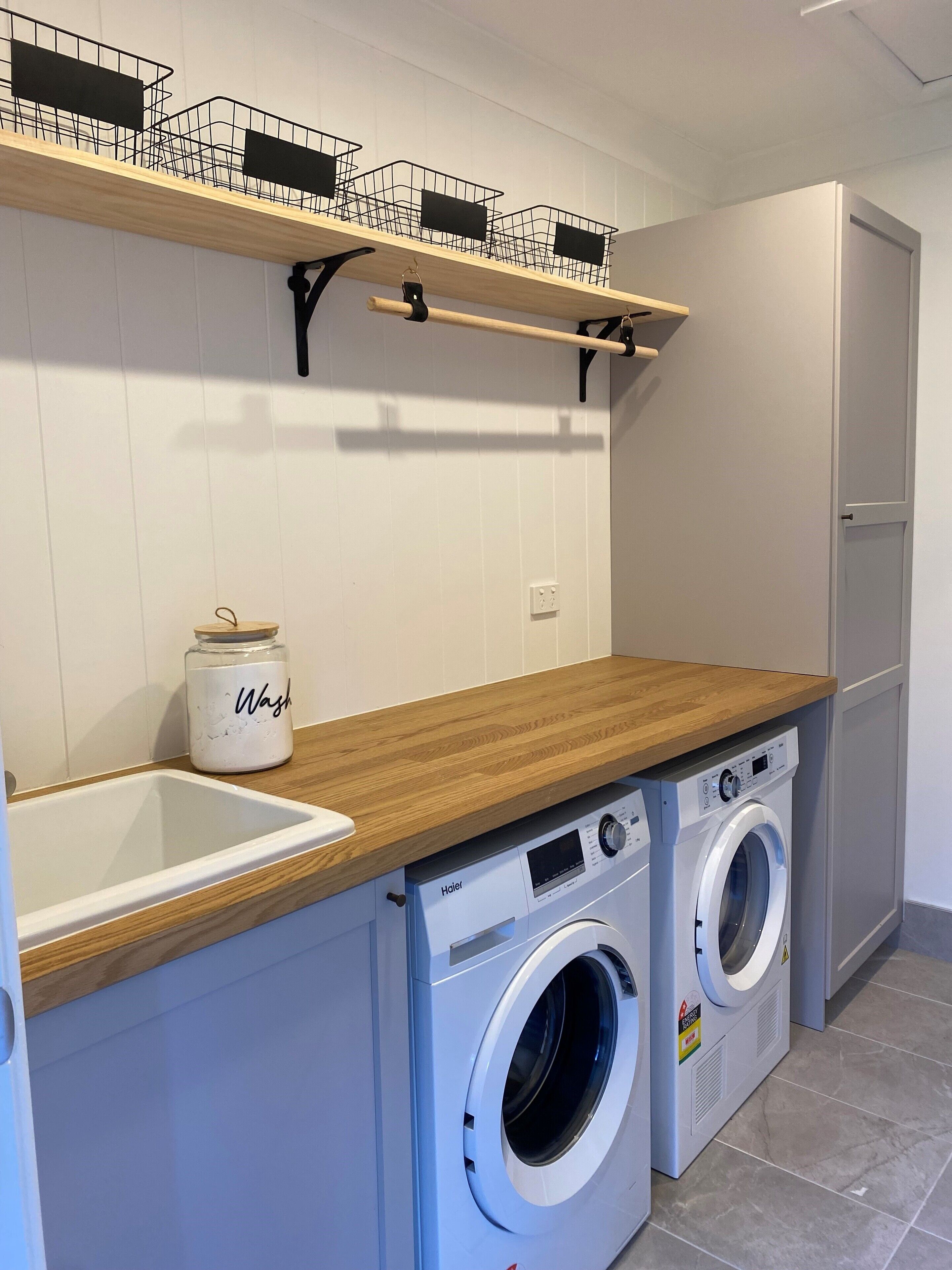Un lavadero con dos lavadoras de carga frontal, una encimera de madera, un lavabo y una estantería con cestas.