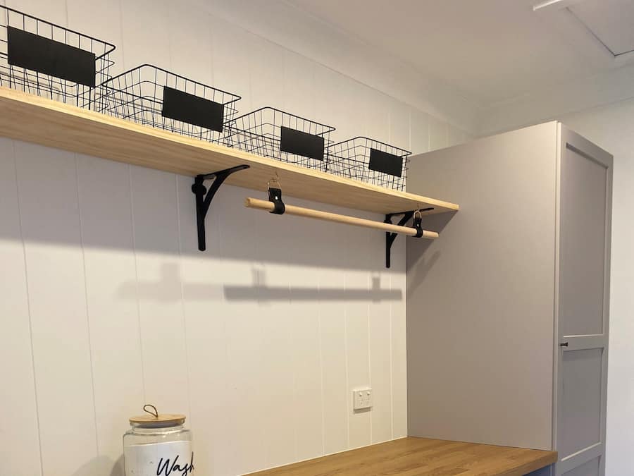 A laundry room with two front-loading washing machines, a wooden countertop, a sink, and a shelf with baskets.