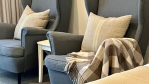 Two grey armchairs with cushions, a small white table, and a patterned throw blanket. - Berrima Bakehouse Motel (Berrima)