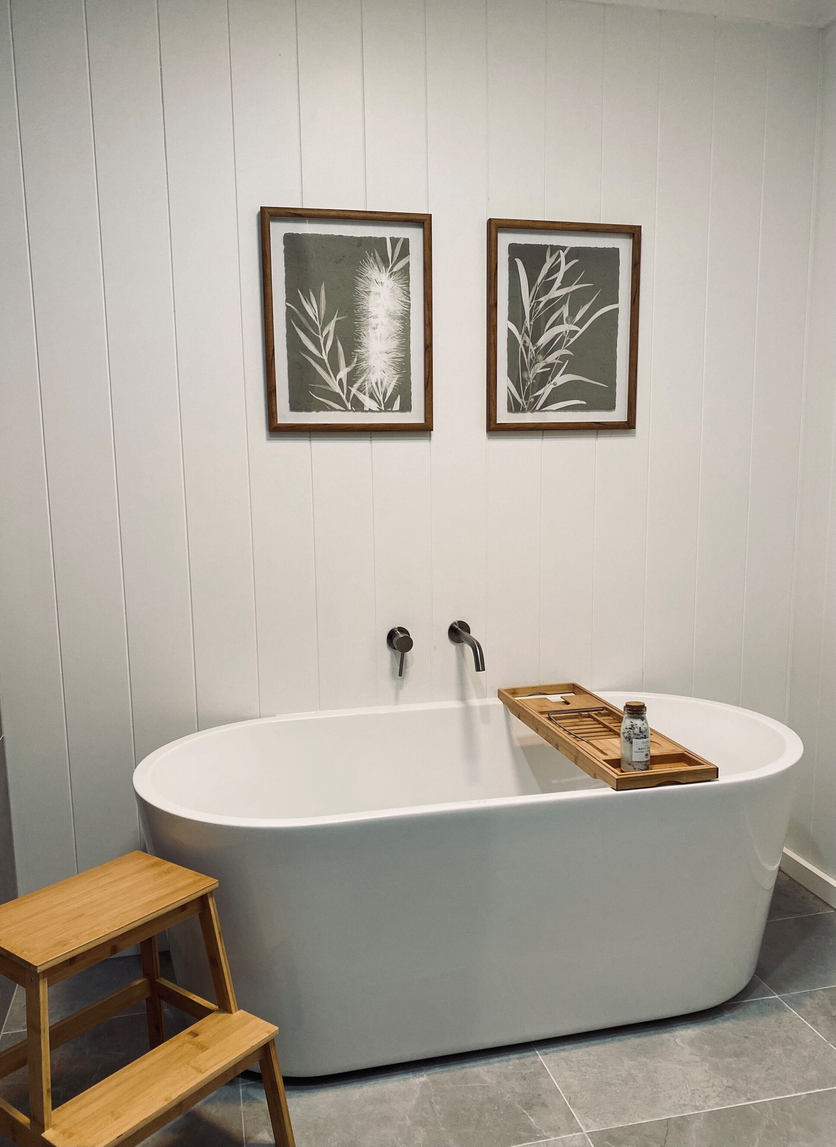 Une salle de bain moderne avec une baignoire sur pieds, des marches en bois et deux reproductions botaniques encadrées accrochées au mur.