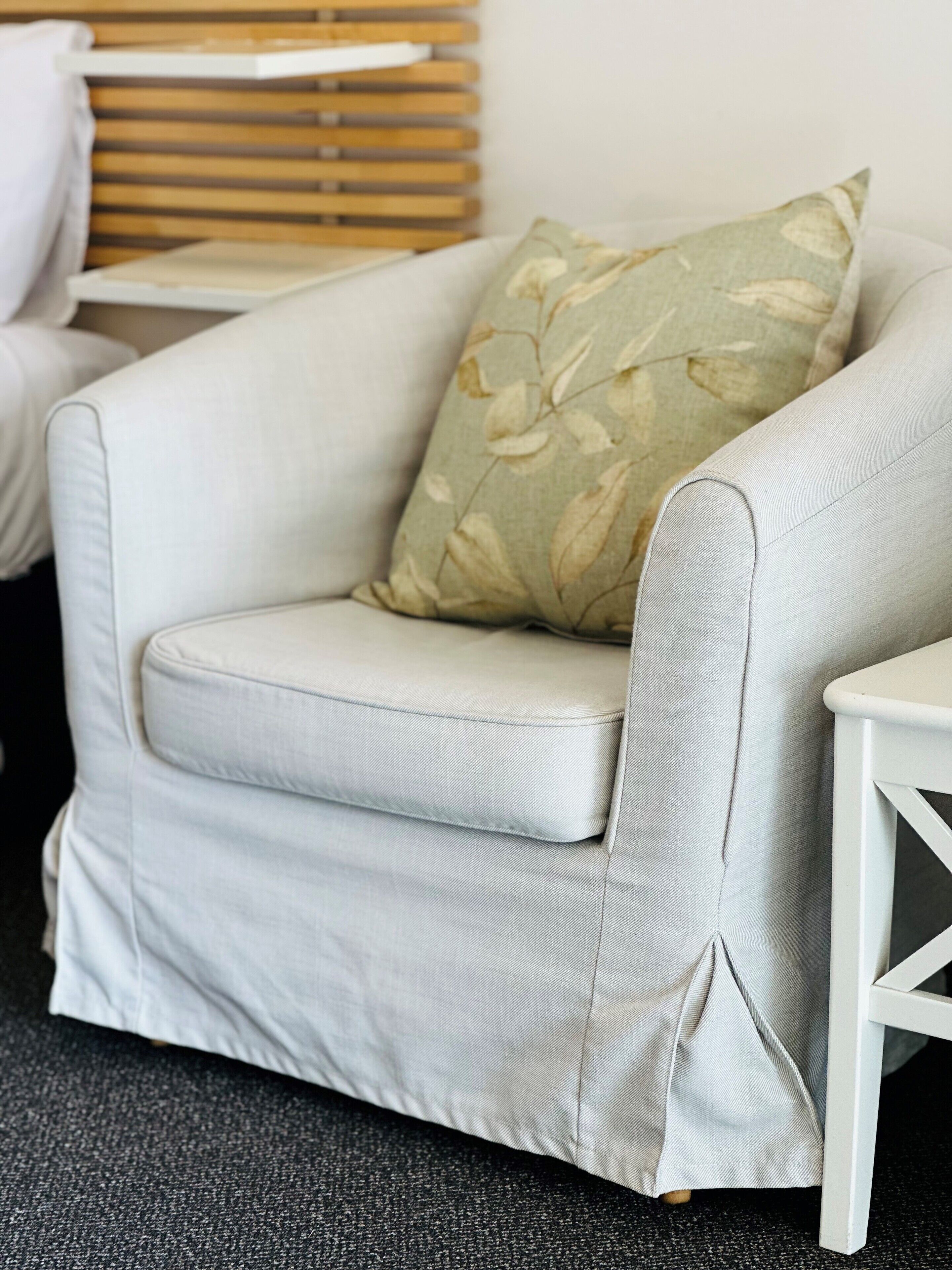 A light grey armchair with a floral pillow, positioned next to a white side table.