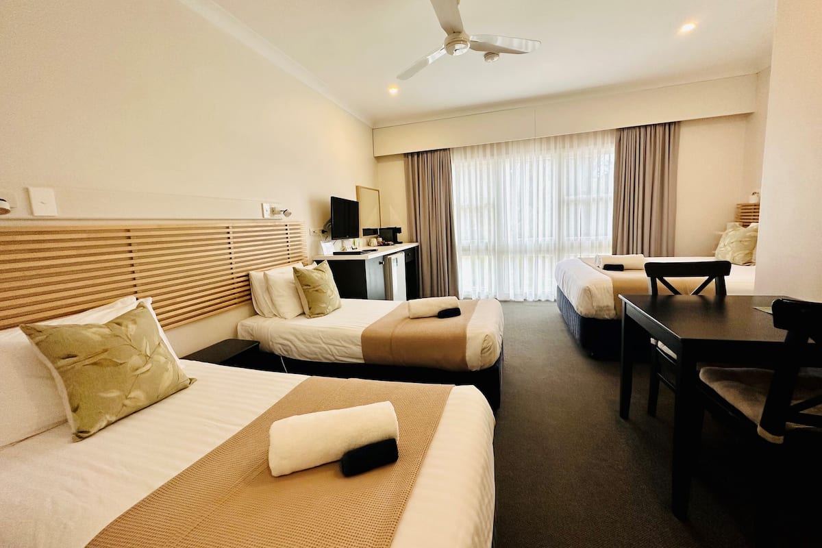 A hotel room with two beds, a desk, a chair, a television, and a ceiling fan.