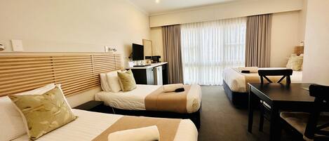 A hotel room with two beds, a desk, a chair, a television, and a ceiling fan.