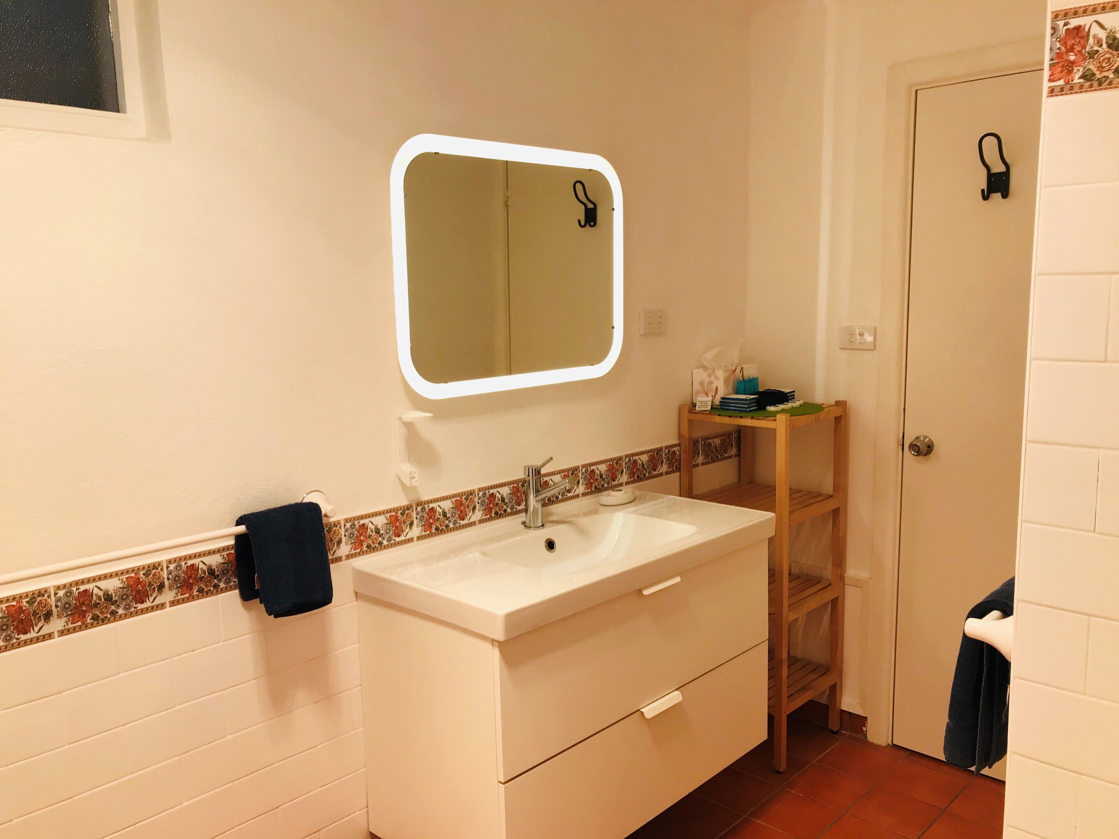 A bathroom with a white sink, a mirror, a towel rack, and a shelf with toiletries.