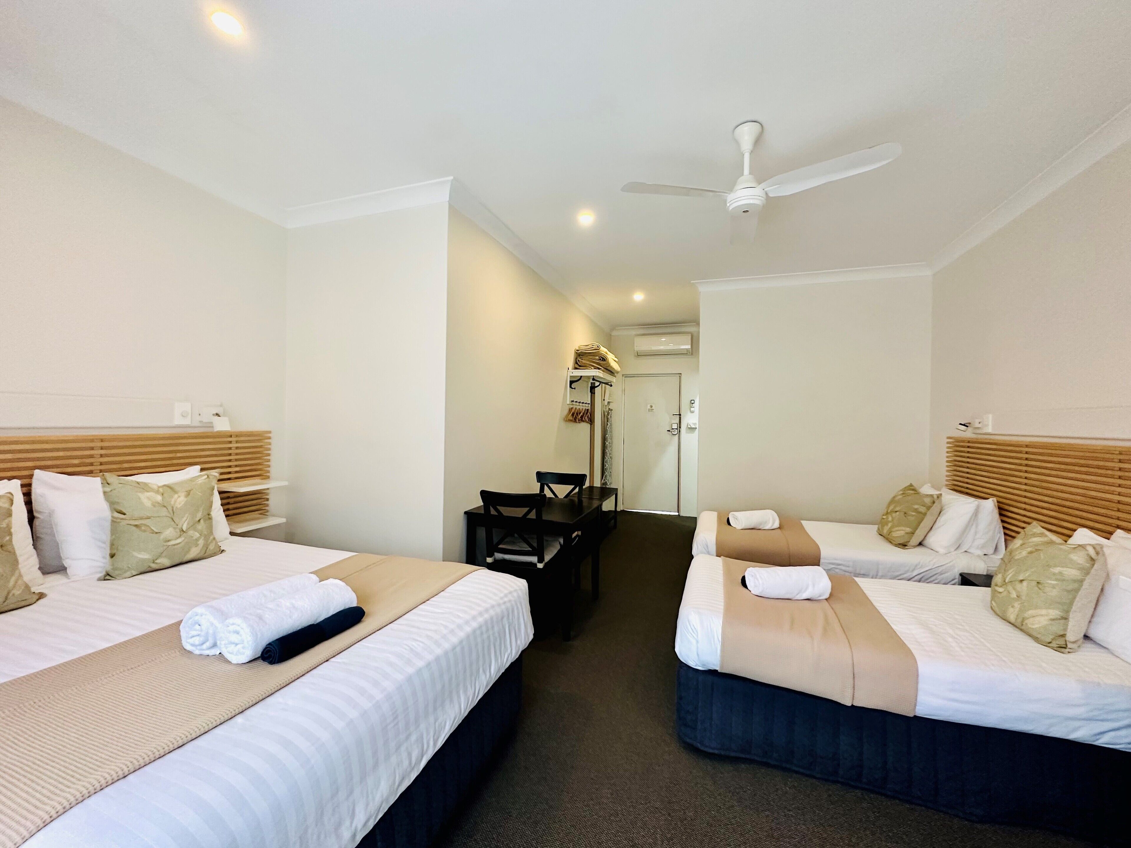 A hotel room with two beds, a desk, and a ceiling fan.