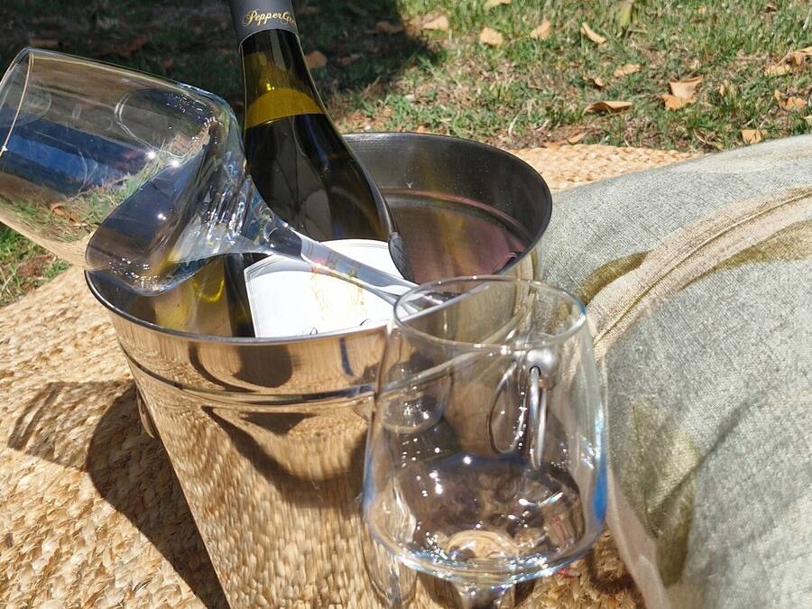 A bottle of wine, a glass, and a wine glass on a woven mat outdoors.
