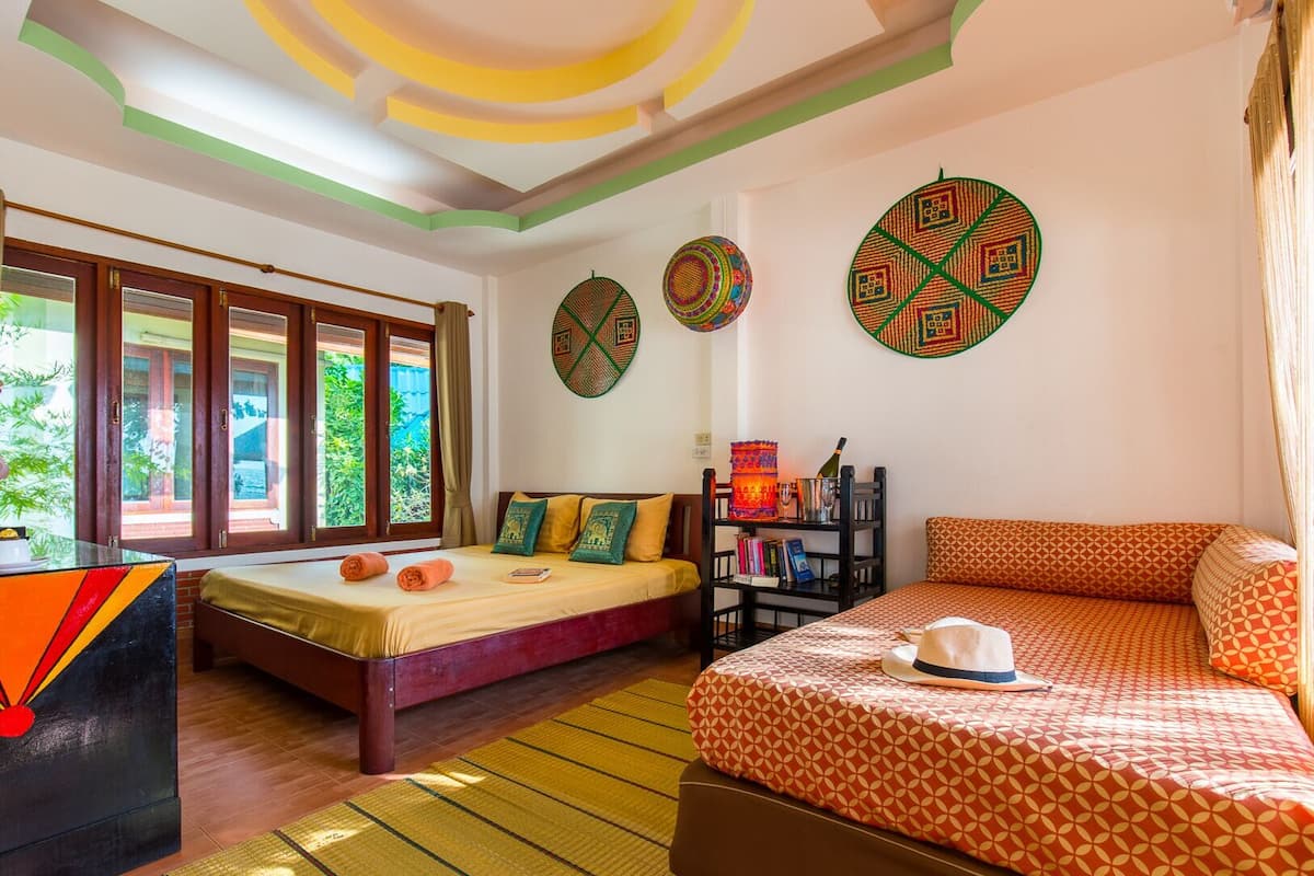 A hotel room with two beds, a wooden desk, a bookshelf, and decorative wall hangings.