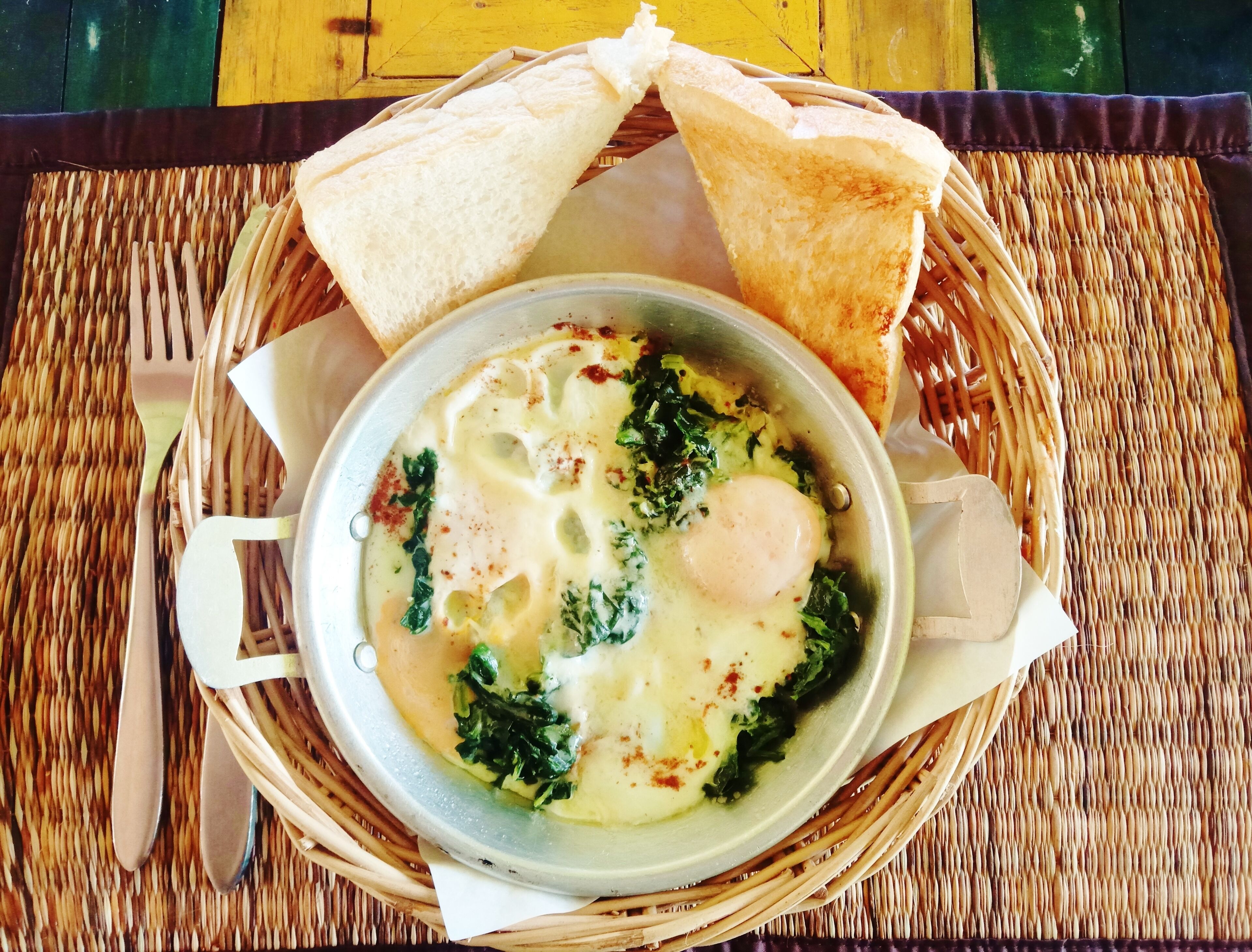 A bowl of soup with a poached egg, spinach, and a slice of toast on a woven mat.