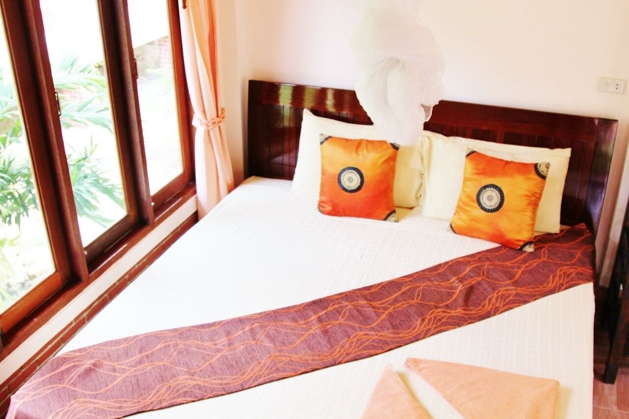 Une chambre d’hôtel avec un grand lit, deux oreillers à motifs circulaires, une tête de lit en bois et une vue sur la verdure par la fenêtre.