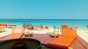 A beachside lounge with orange lounge chairs and tables, a clear view of the ocean, and a calm sea. - Seaboard Bungalows (Ko Pha-ngan)