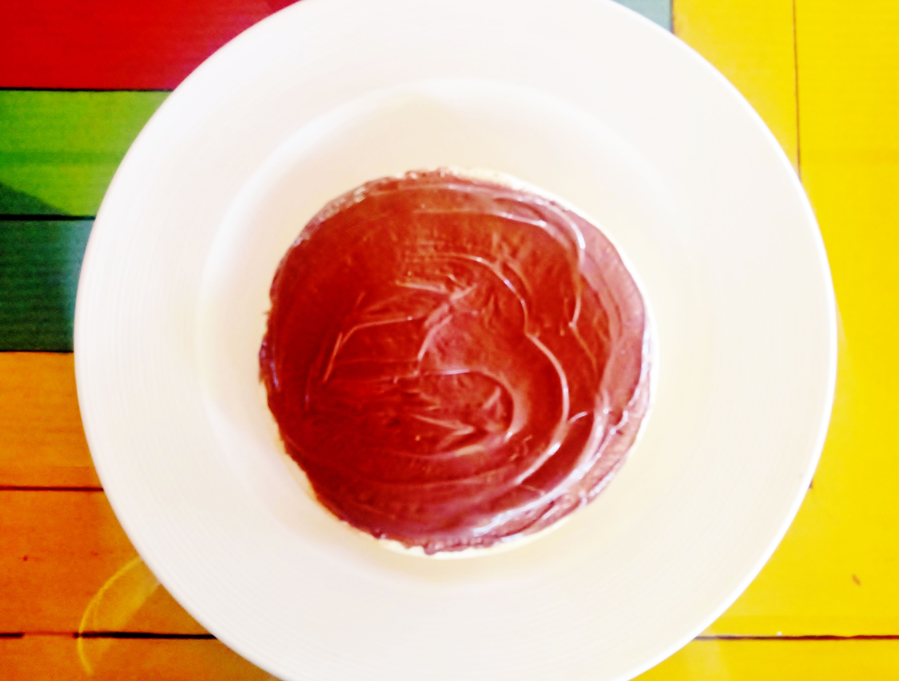 A white plate with a red substance on a colorful wooden surface.