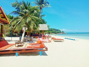 A beachside resort with lounge chairs, a thatched-roof structure, and palm trees. - Seaboard Bungalows (Ko Pha-ngan)