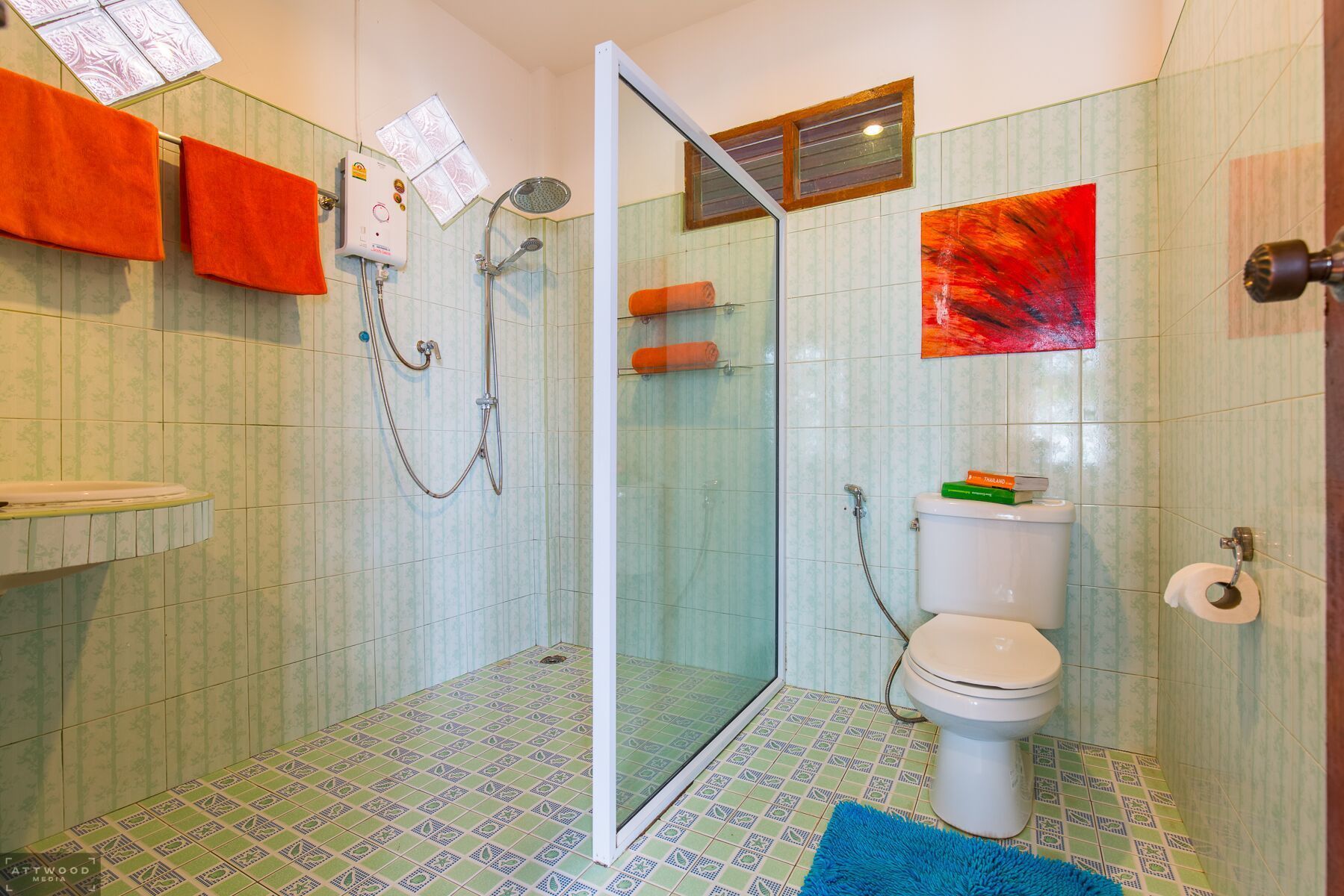 Un baño con ducha, inodoro y lavabo. Hay toallas colgadas en la pared y un libro sobre el inodoro.