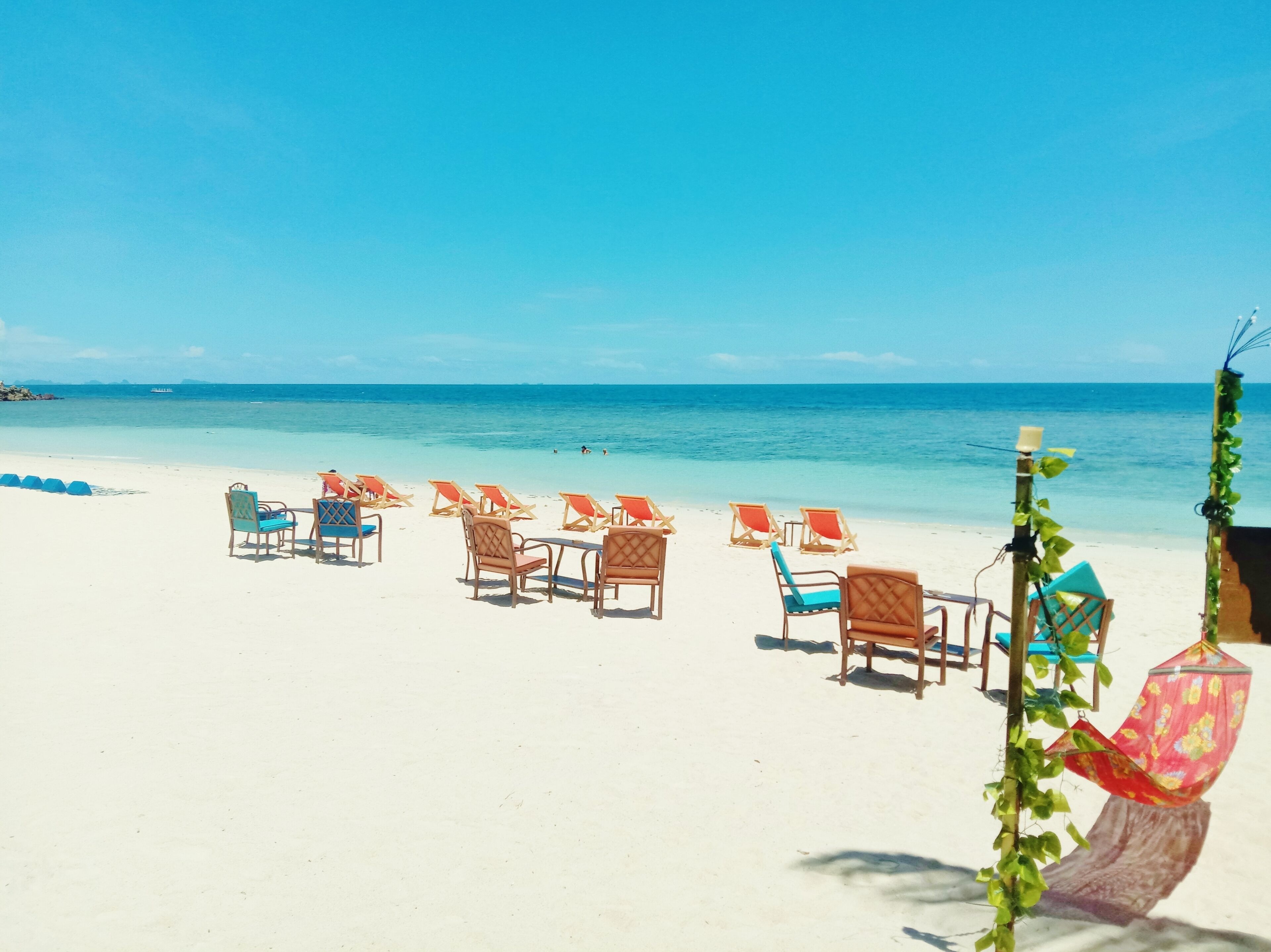 A beach with rows of wooden lounge chairs and a hammock.