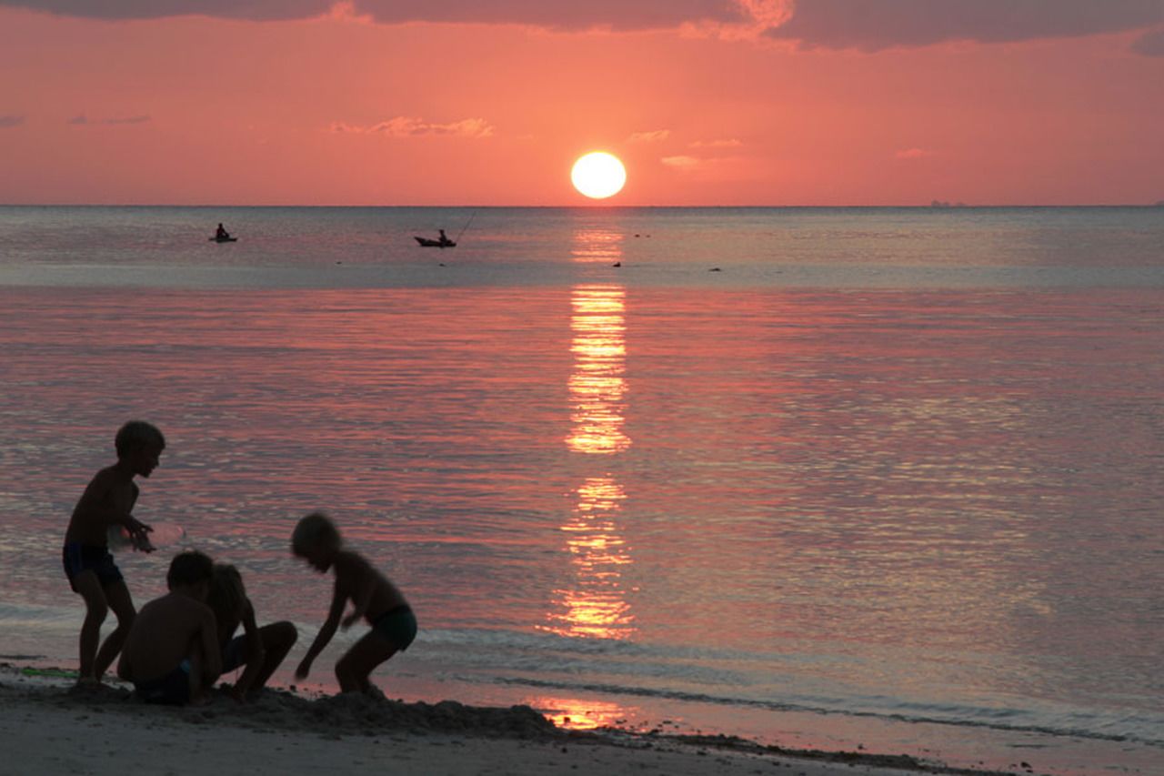 A sunset over a beach with people playing in the sand.