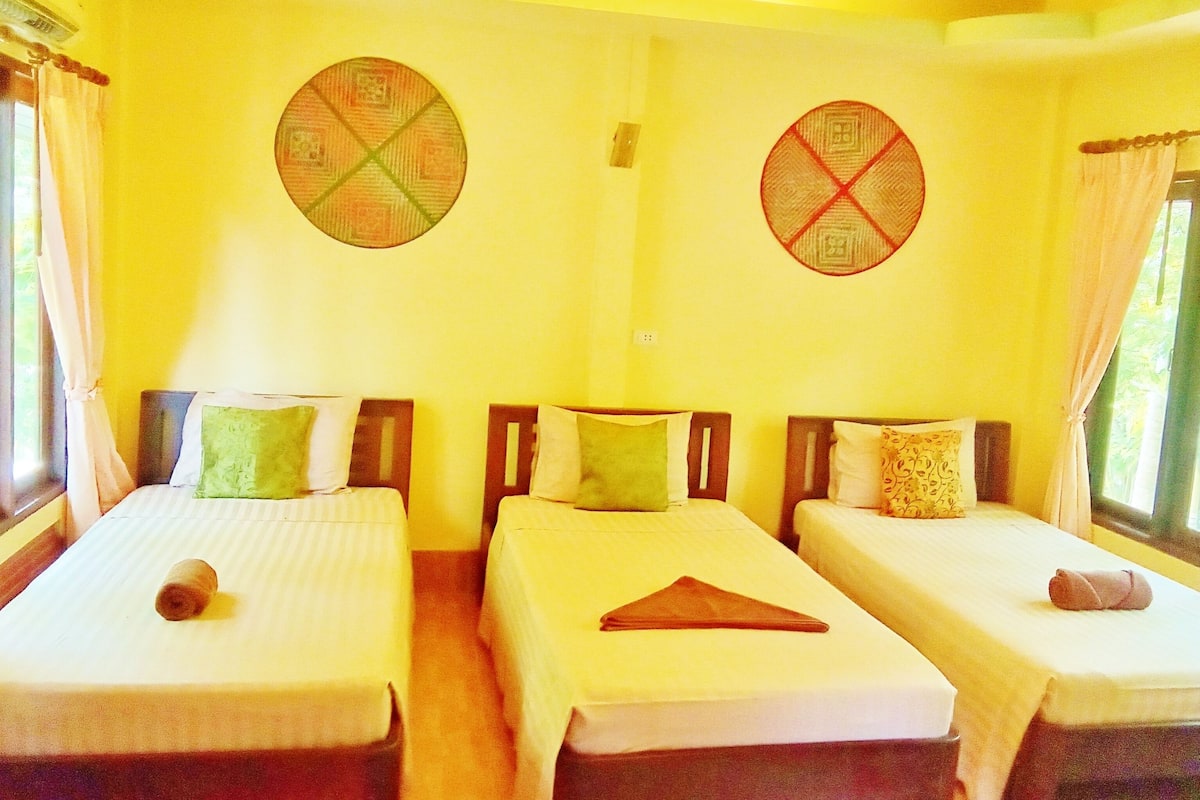 A room with three single beds arranged in a row, each with a pillow and a rolled towel.