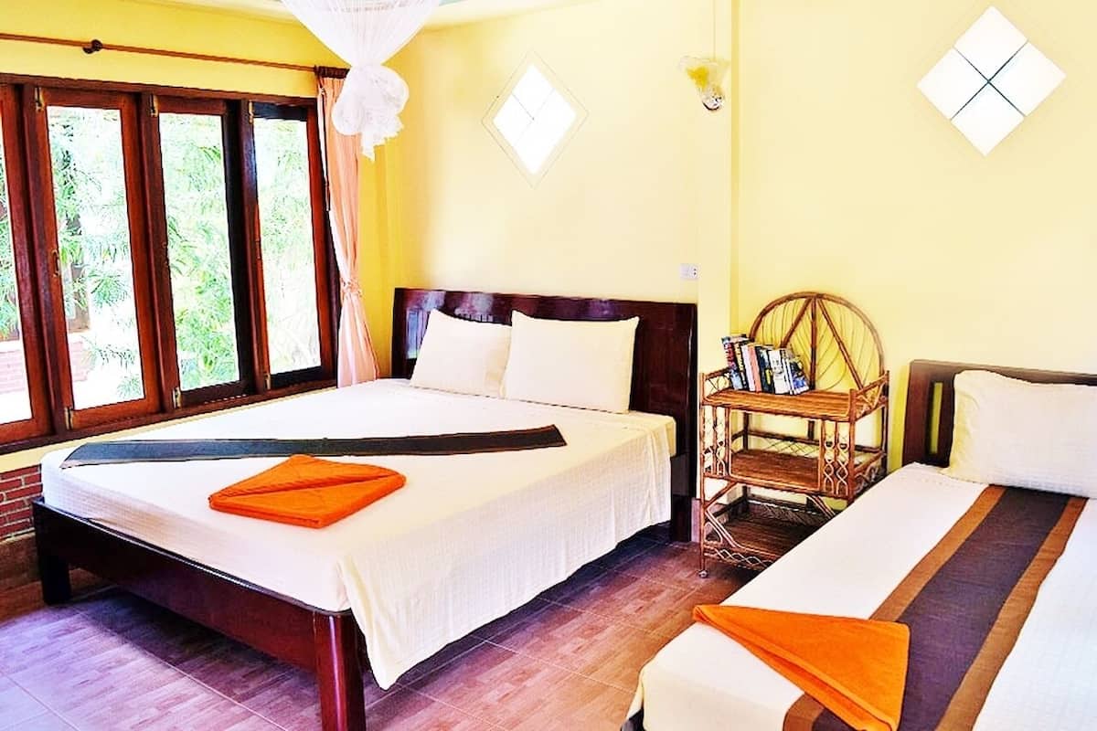 A hotel room with a large bed, a smaller bed, a wooden side table, and a window with curtains.