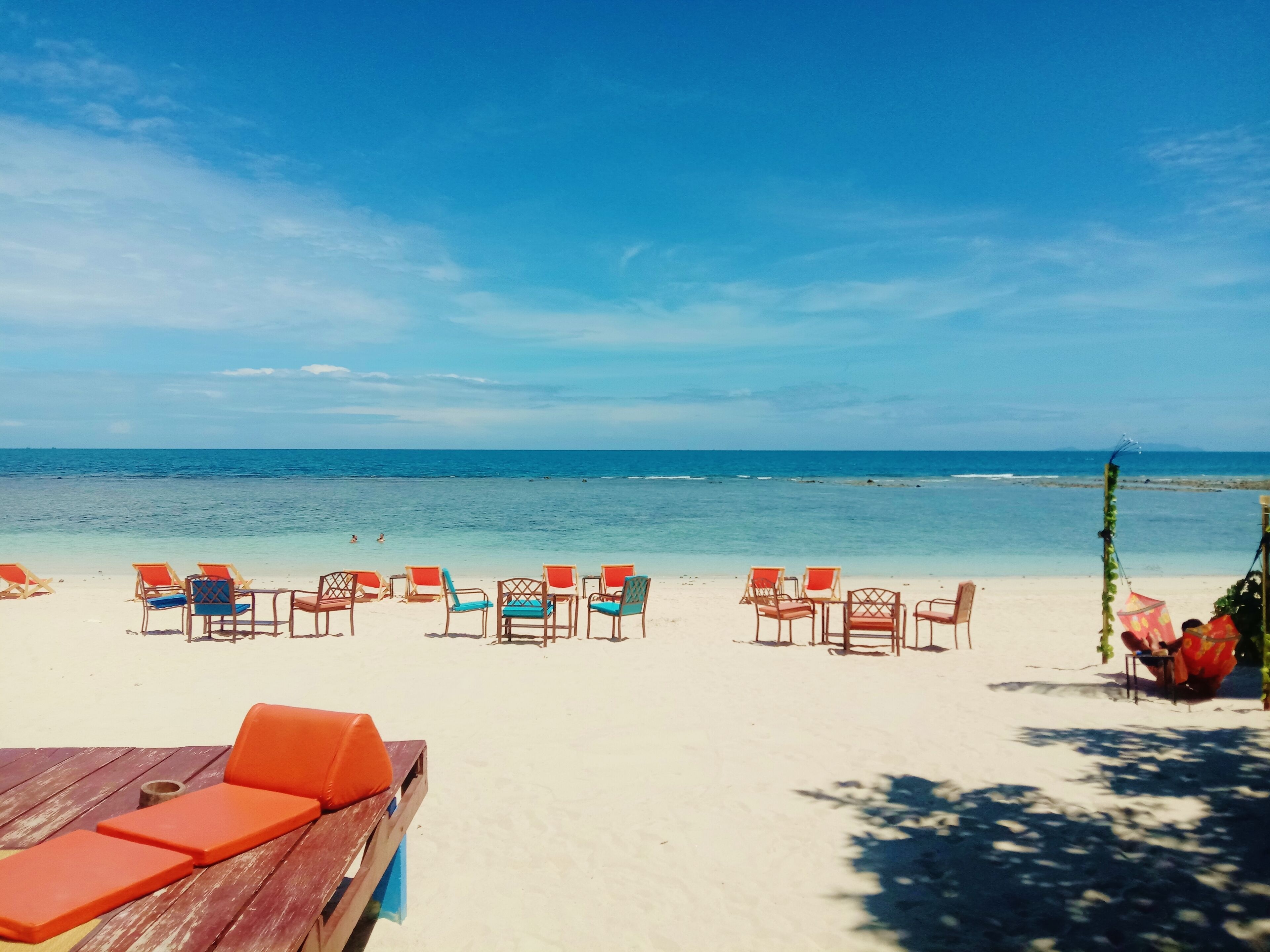 A beach with rows of colorful chairs and a wooden table, suggesting a beachside seating area.