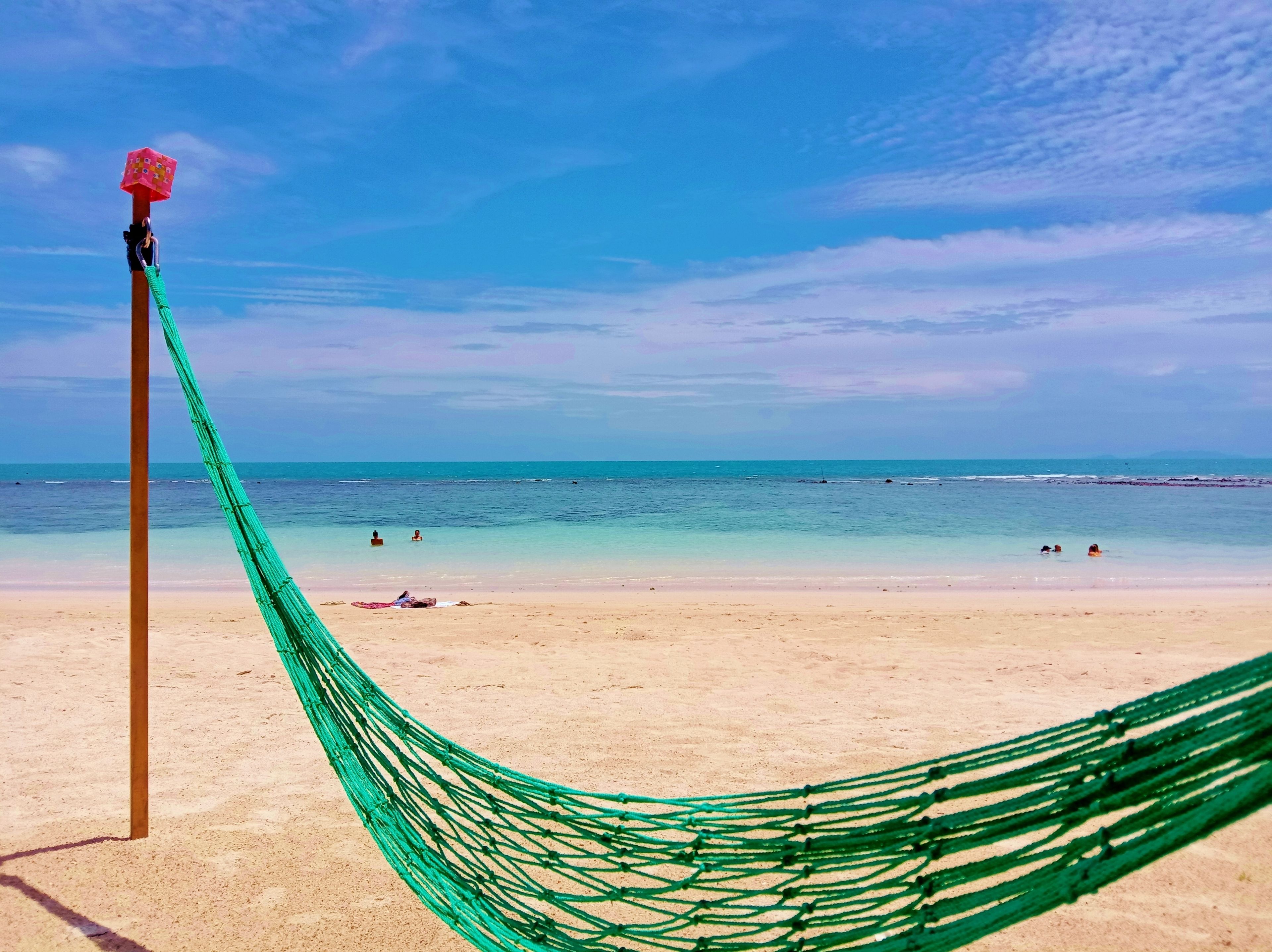 A beach scene with a hammock tied to a pole, clear blue sky, and calm sea.