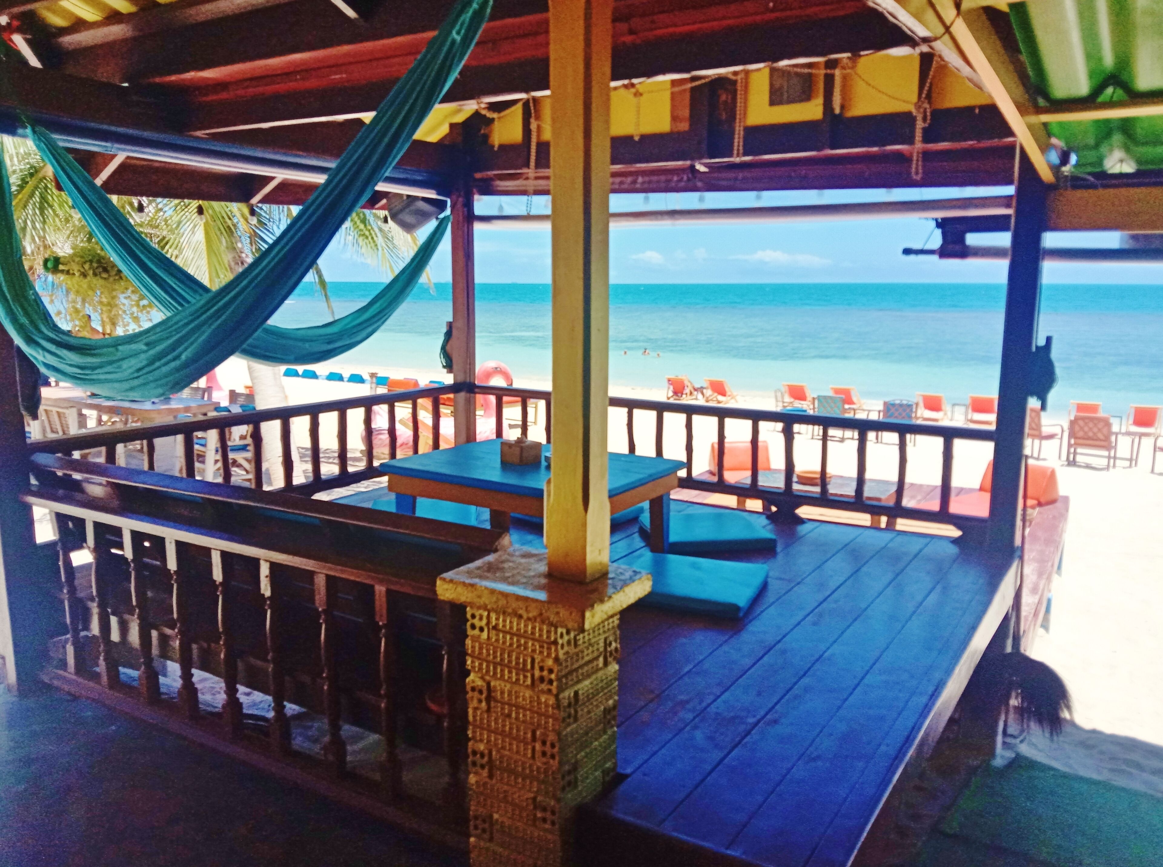 A beachside patio with wooden tables and benches, overlooking the ocean.