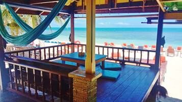 A beachside patio with wooden tables and benches, overlooking the ocean.