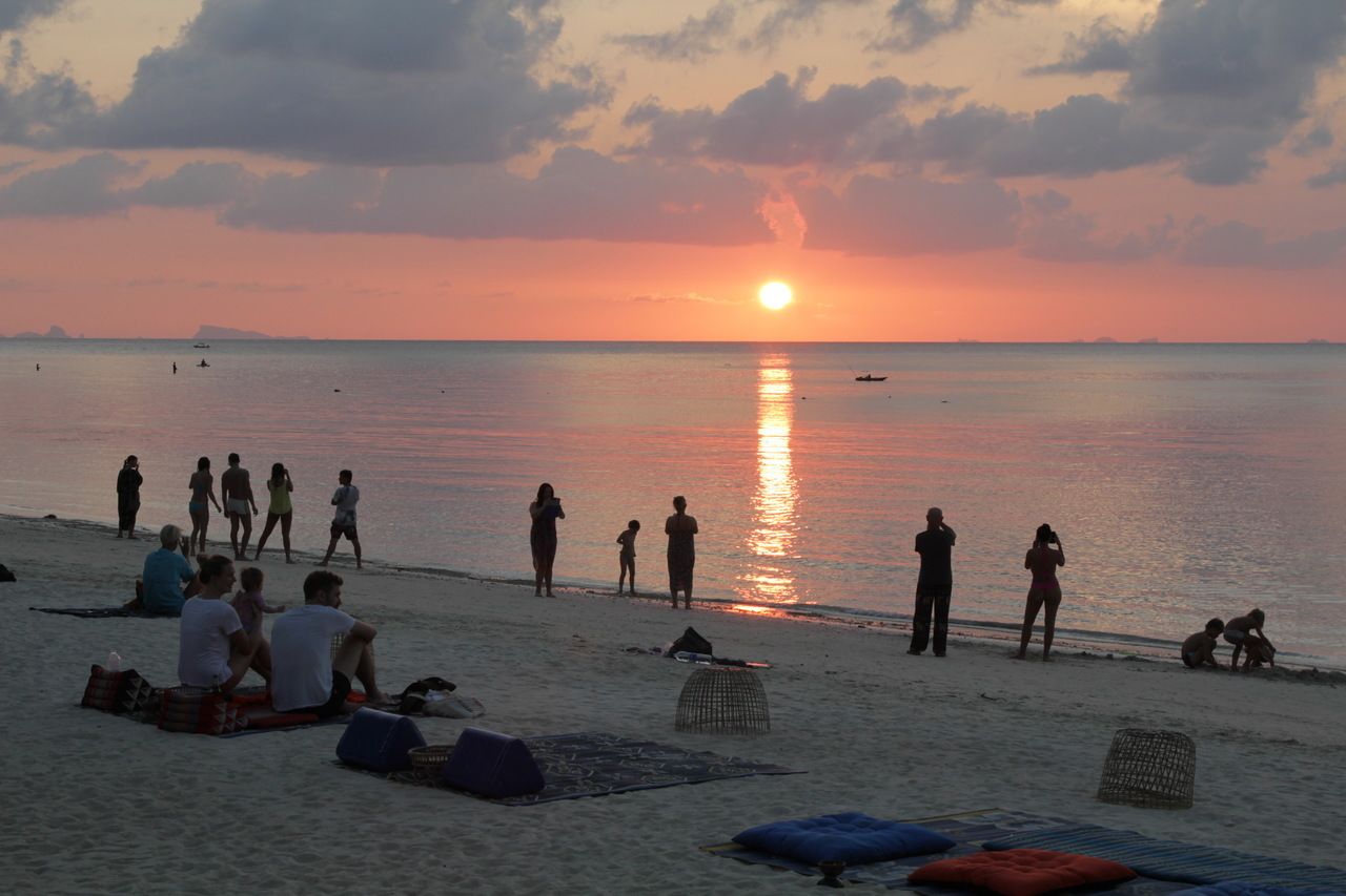 Een strand bij zonsondergang, mensen ontspannen en wandelen langs de kust.
