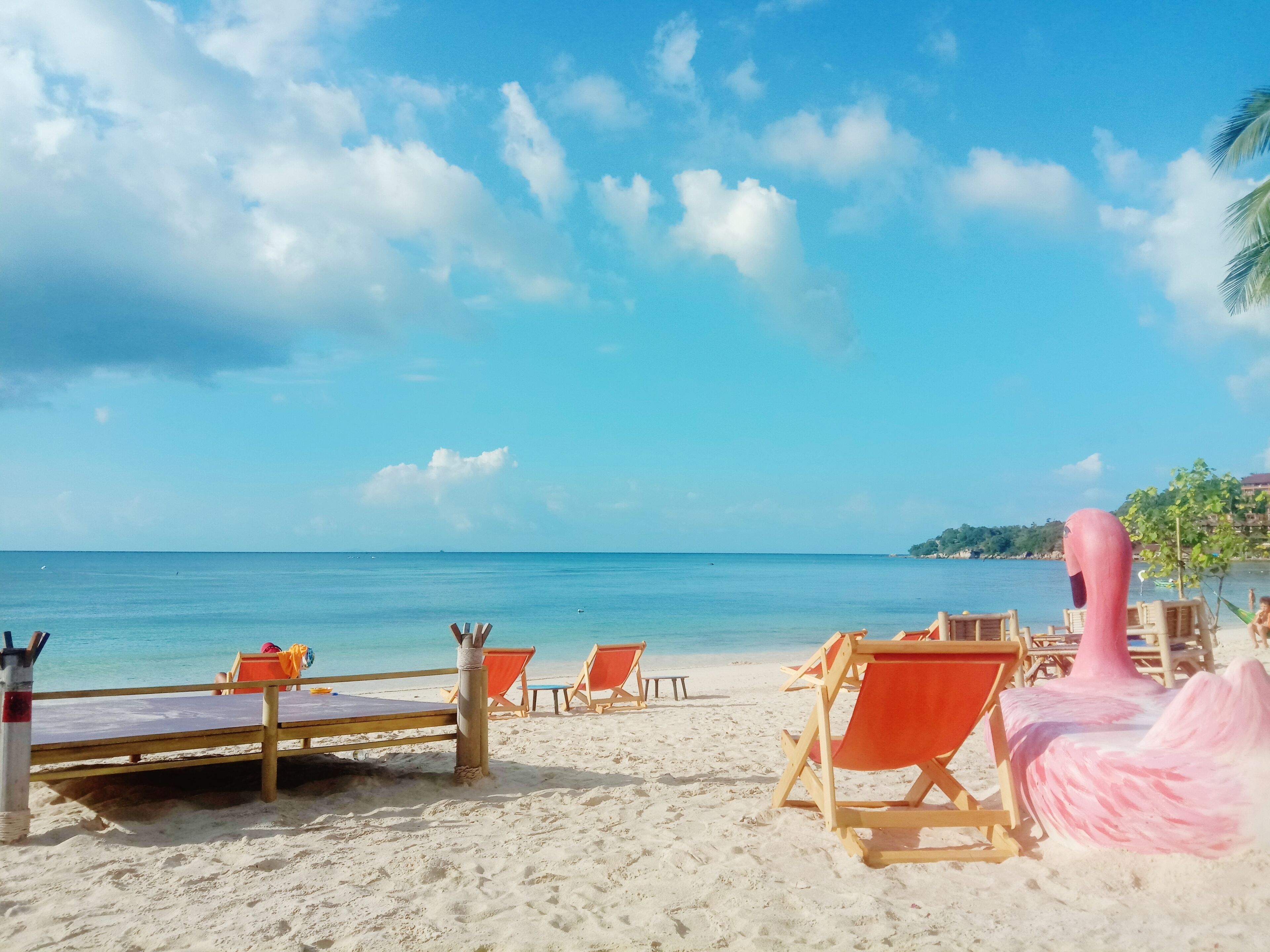 A beach with wooden lounge chairs and a pink flamingo statue.