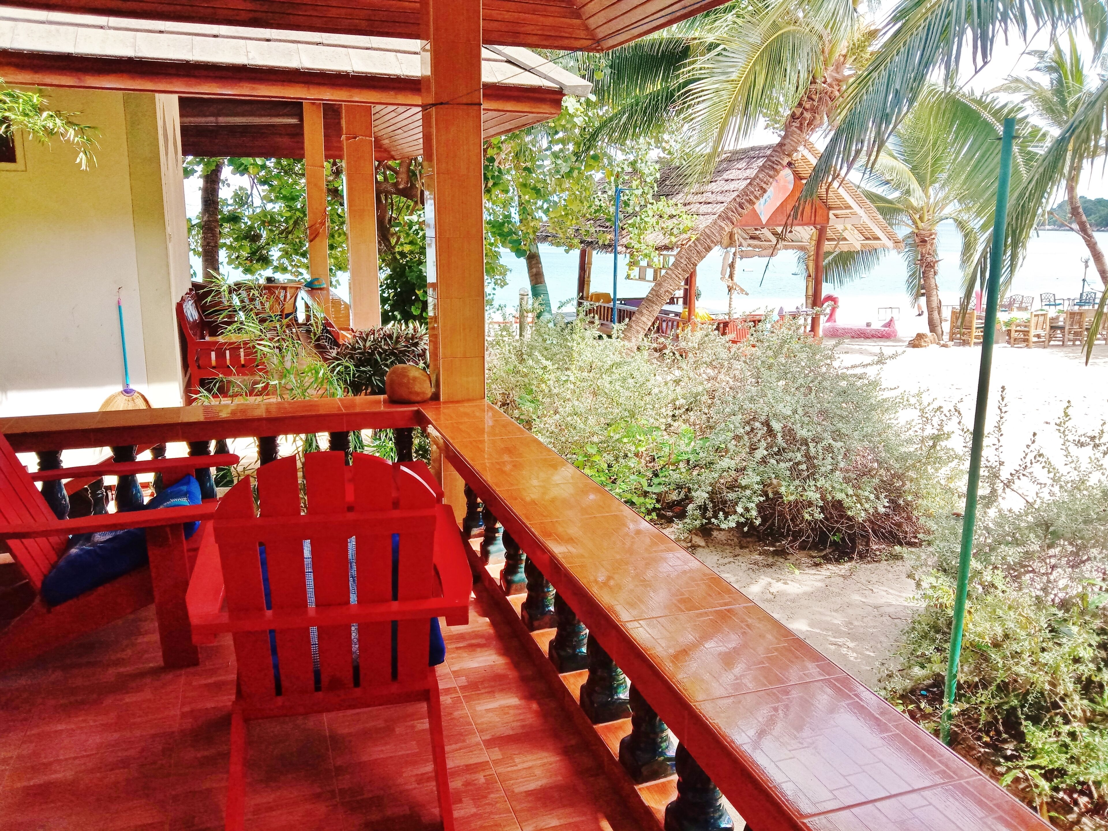 A wooden deck with red chairs, a view of the beach, and palm trees.