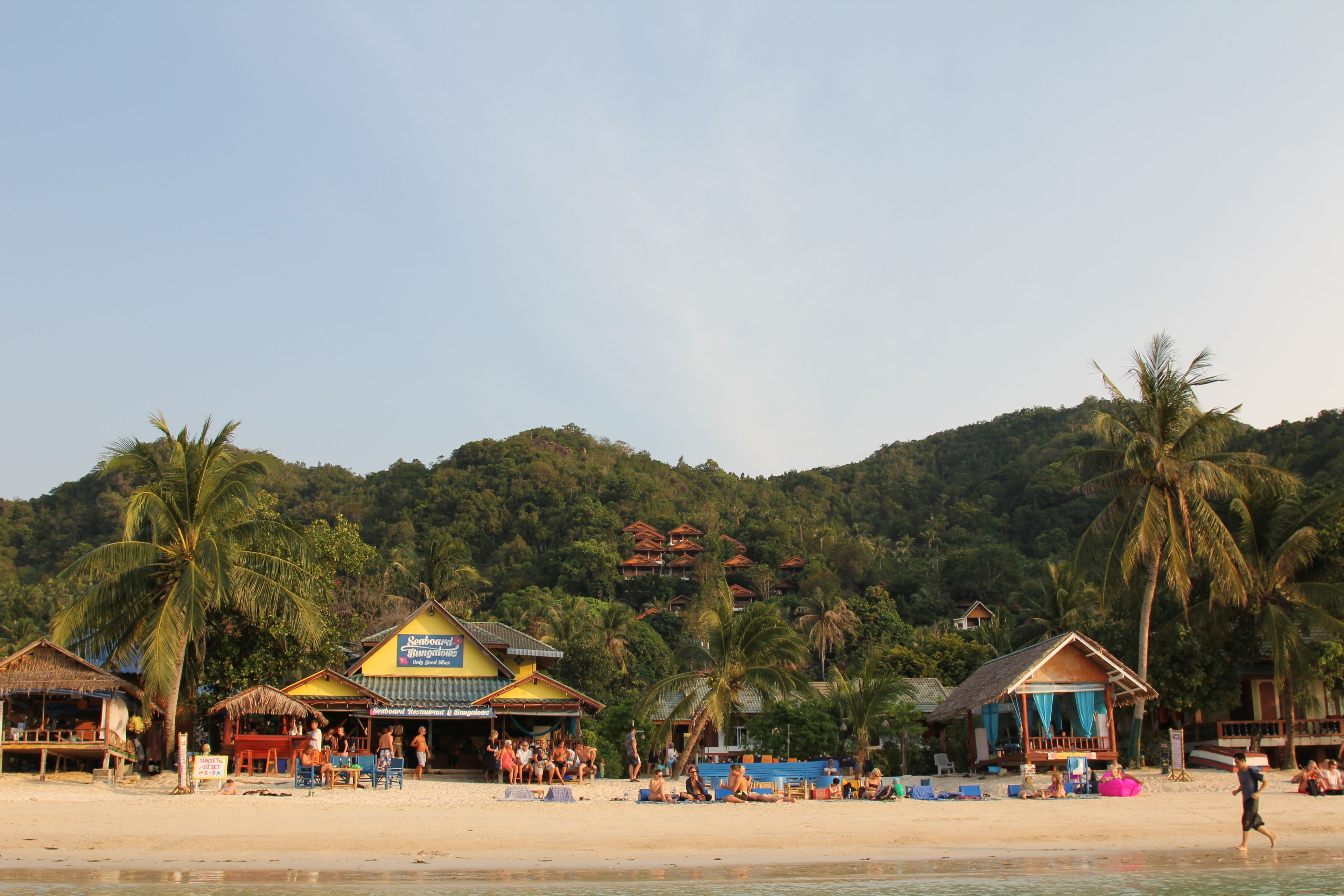 A beach with several small huts and a larger building with a sign.