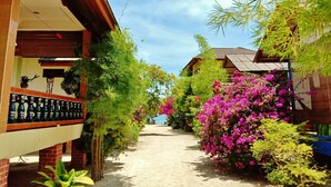 A pathway flanked by buildings with a covered area on the left and a garden with vibrant flowers on the right. - Seaboard Bungalows (Ko Pha-ngan)